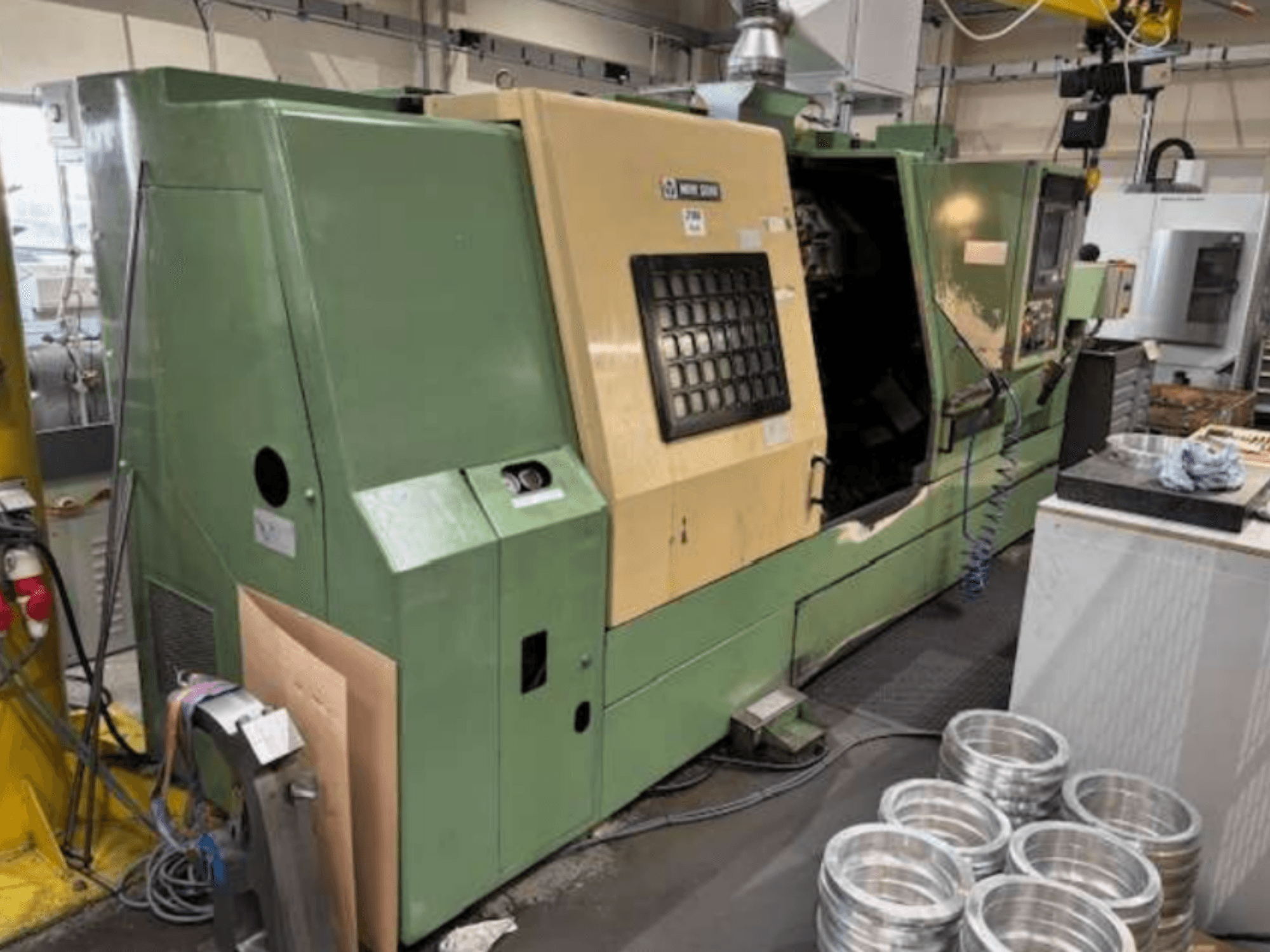 Torno CNC verde da Mazak, visto de frente, apresentando um painel de controlo e peças de alumínio maquinadas numa mesa de trabalho.