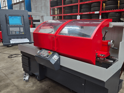 Torno CNC vermelho com painel de controlo, vista frontal; possui tampa transparente, suporte de ferramentas e gavetas de arrumação.