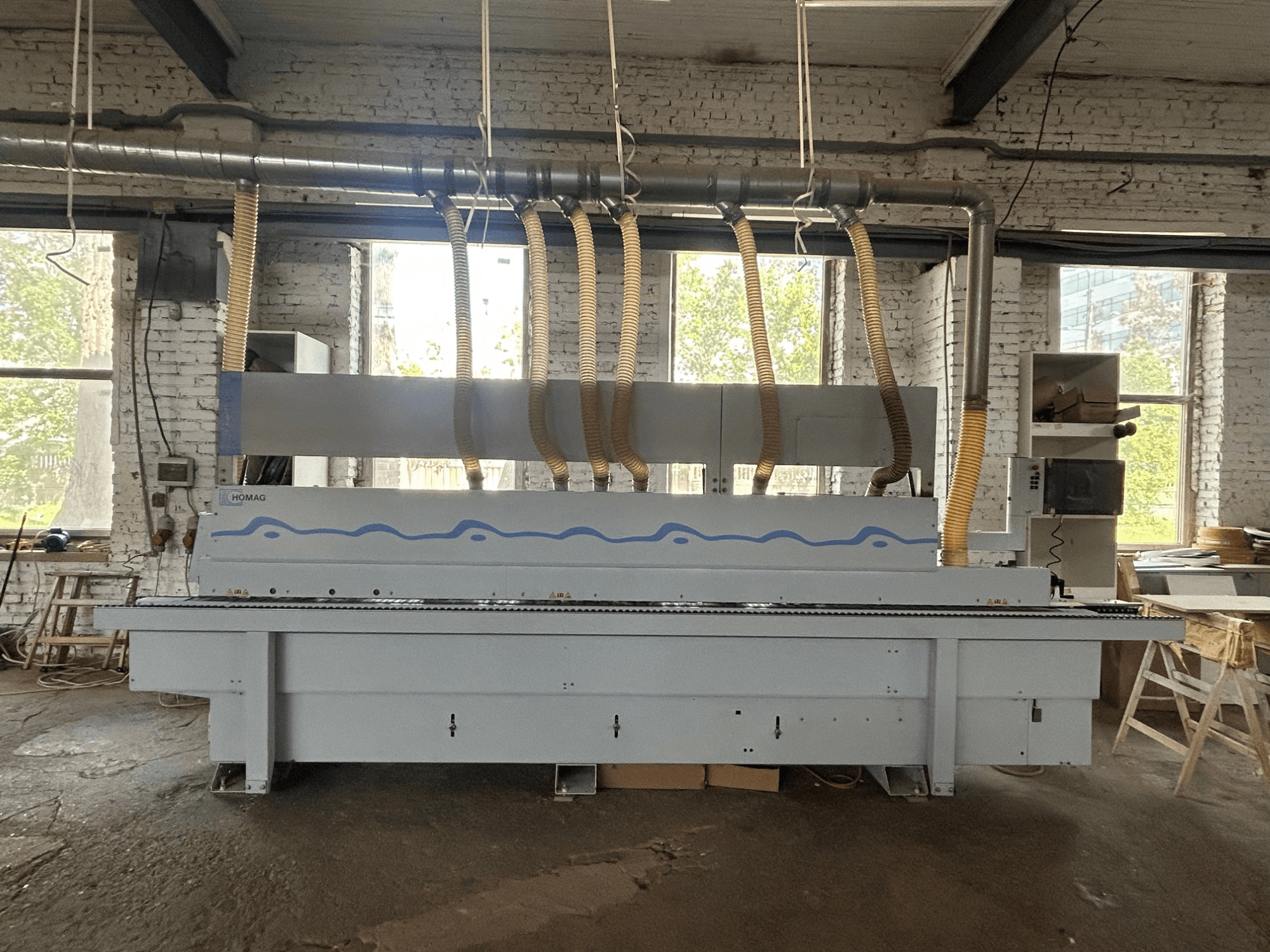 Vista frontal da encoladora HOMAG Optimat KDF 440 C, mostrando uma máquina de grandes dimensões com mangueiras de extração de pó e um painel de controlo.