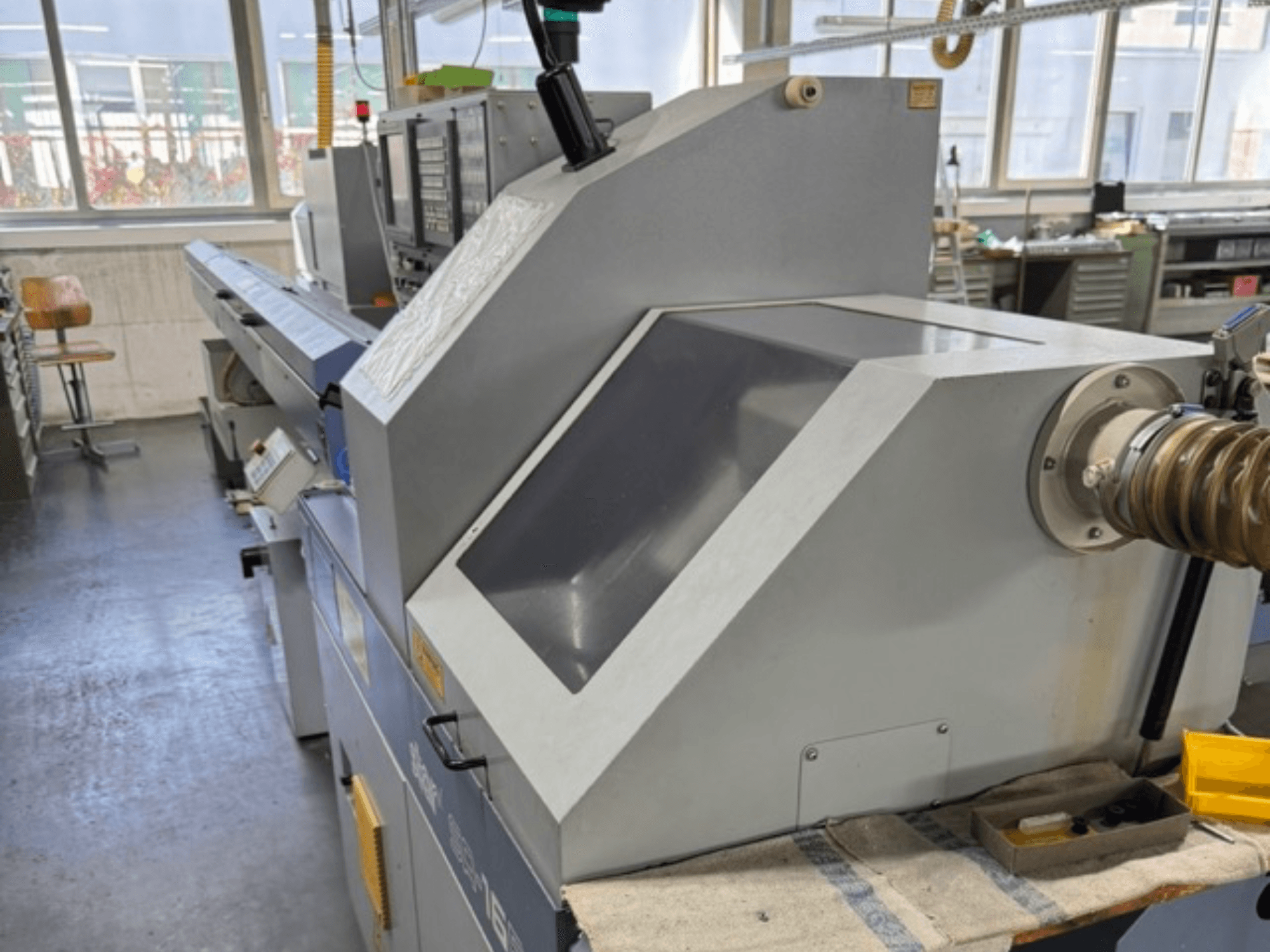 Máquina industrial cinzenta vista de lado, com um grande painel angular, botões de controlo e um acessório para mangueira.