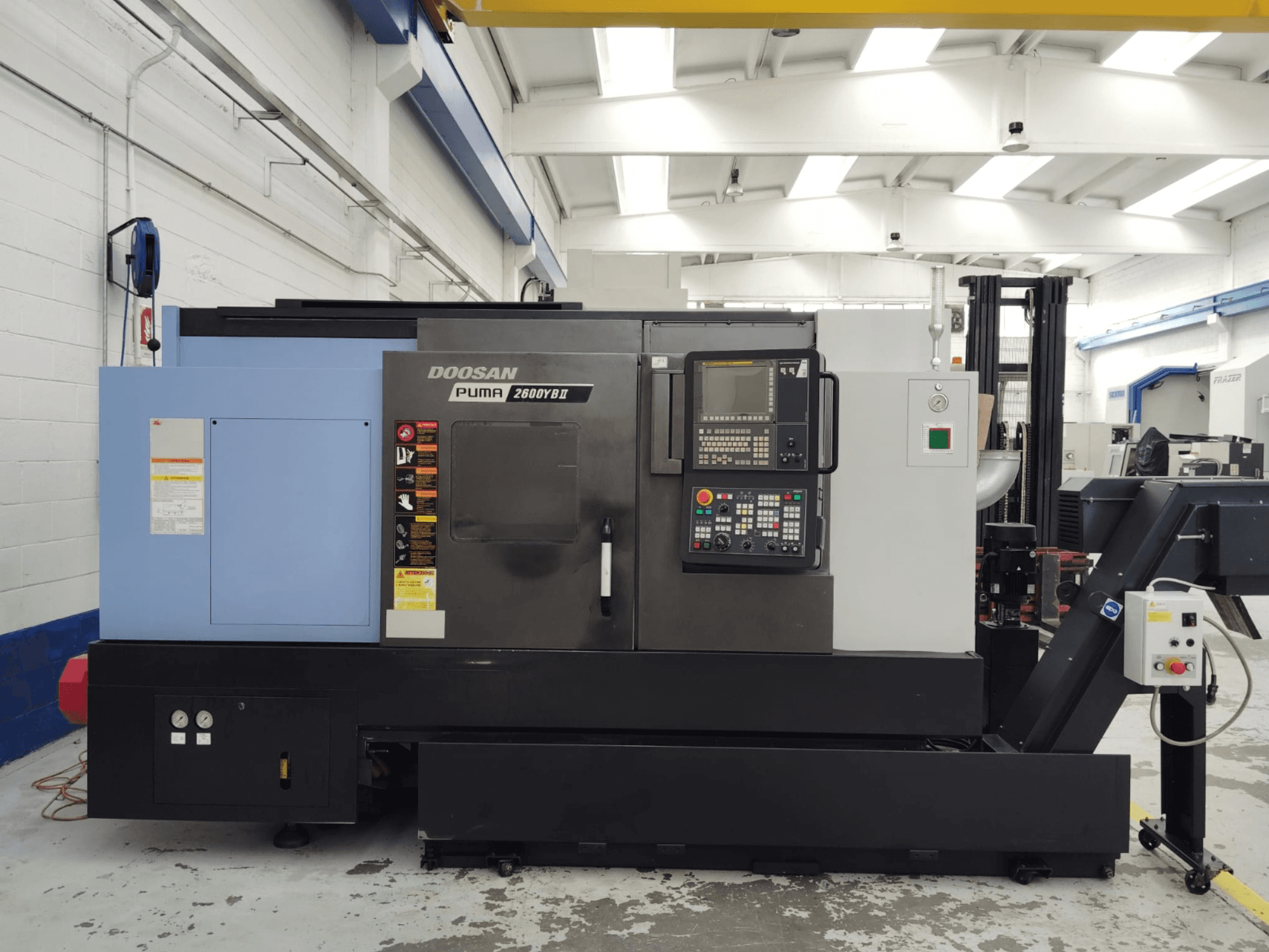 Vista frontal do virador horizontal DOOSAN Puma 2600YB II com o painel de controlo e as etiquetas de segurança visíveis.