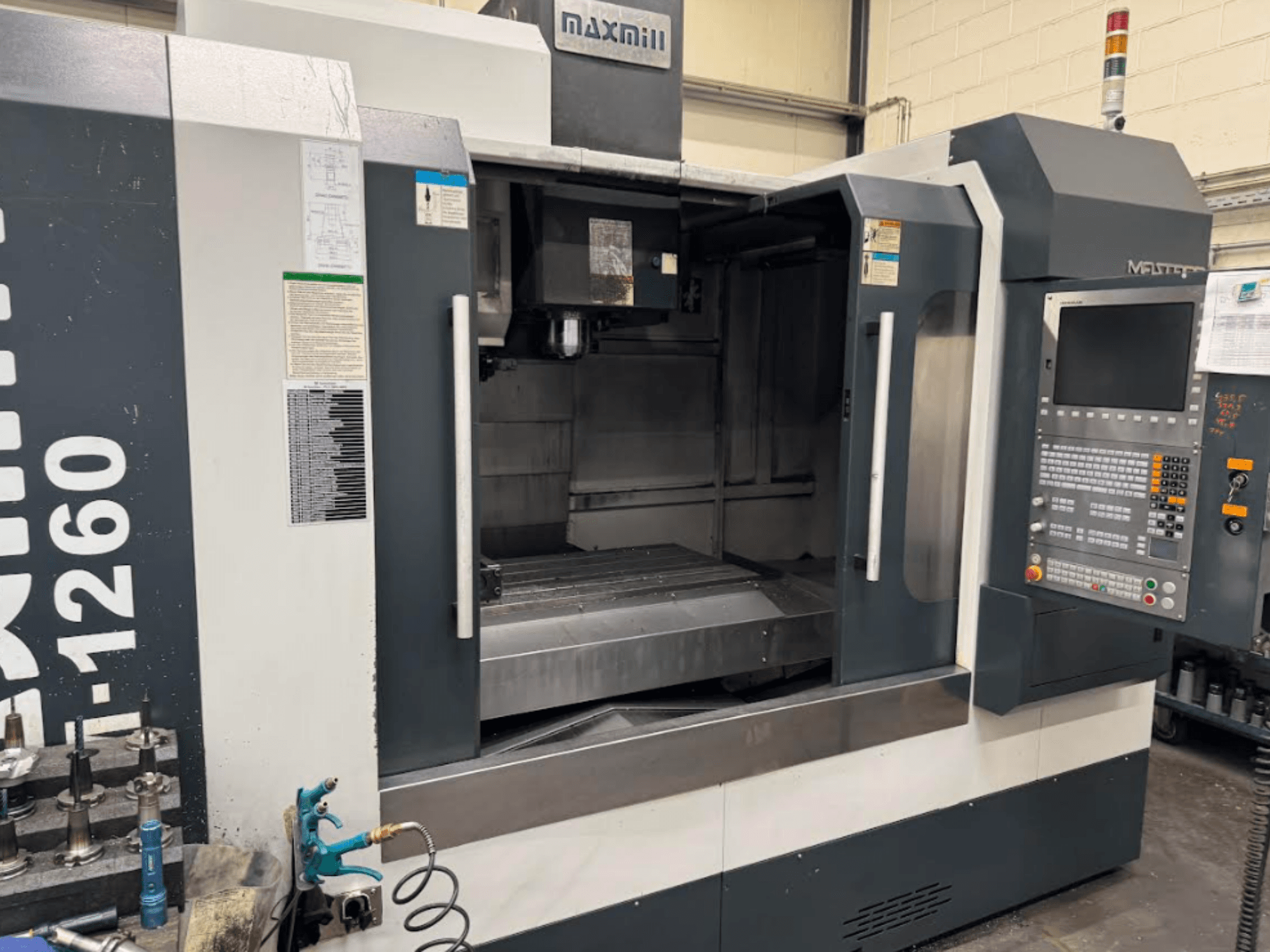 Fresadora Maxmill CNC, modelo M-1260, vista frontal mostrando uma área de trabalho vazia com painel de controlo e instruções de funcionamento.