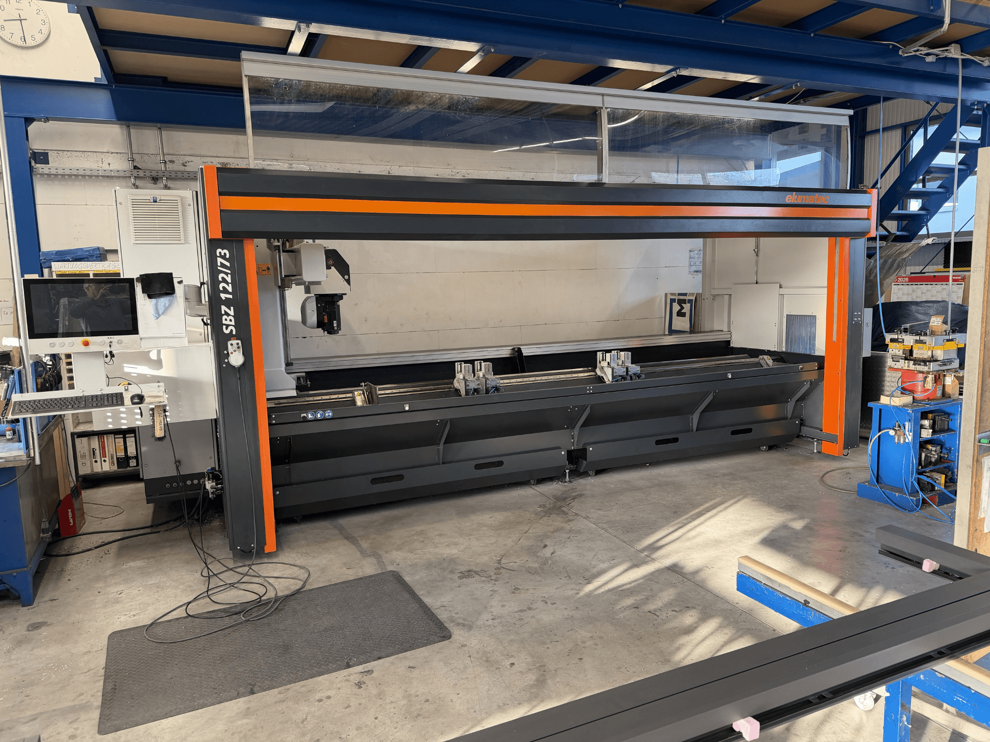Máquina-ferramenta Elumatec SBZ 122/73 em vista frontal, mostrando o painel de controlo, a área de corte e a disposição do espaço de trabalho.