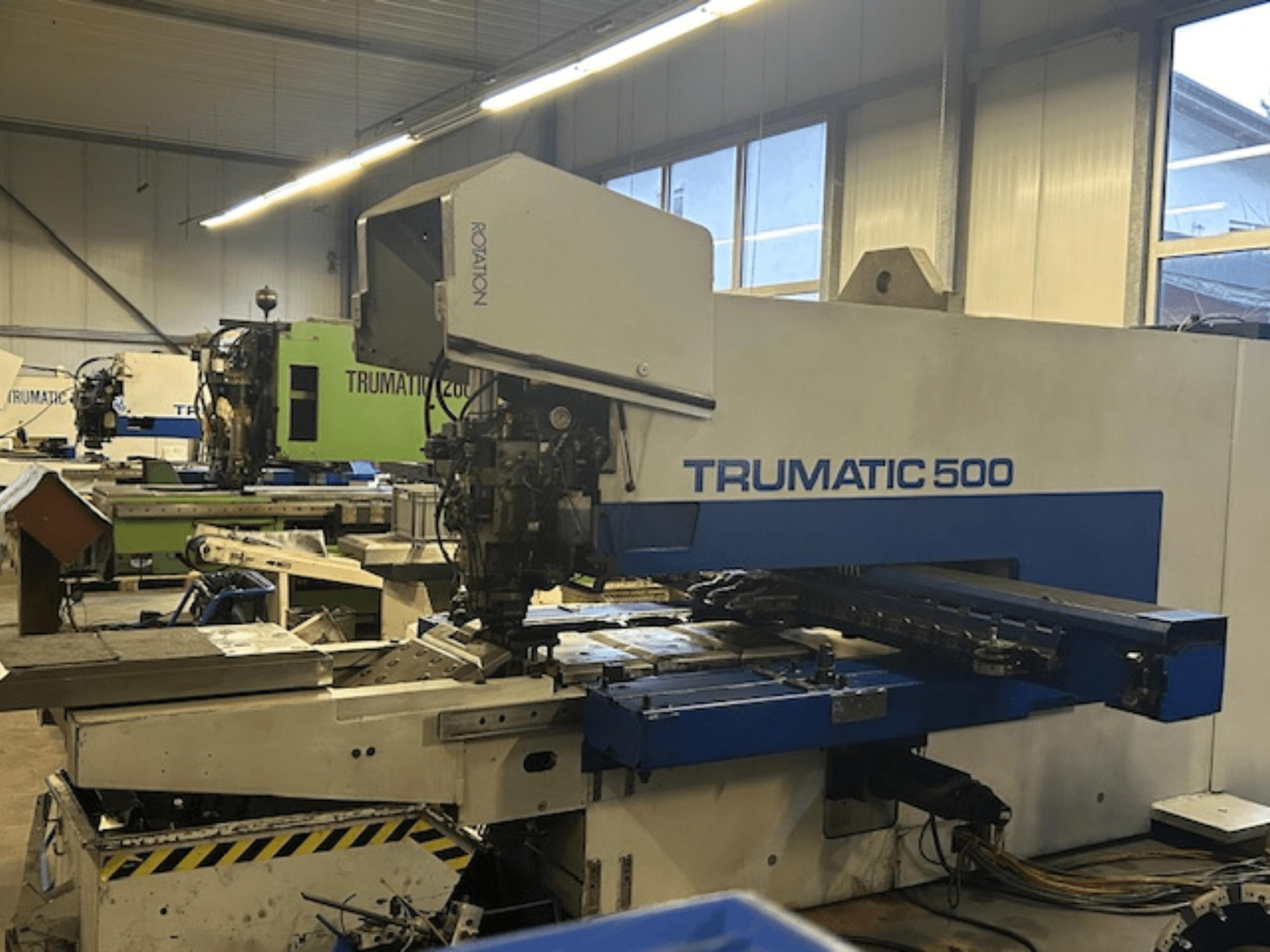 Máquina de puncionar TRUMPF TRUMATIC 500 CNC, vista frontal, com painel de controlo e peças mecânicas. Ambiente de oficina industrial.