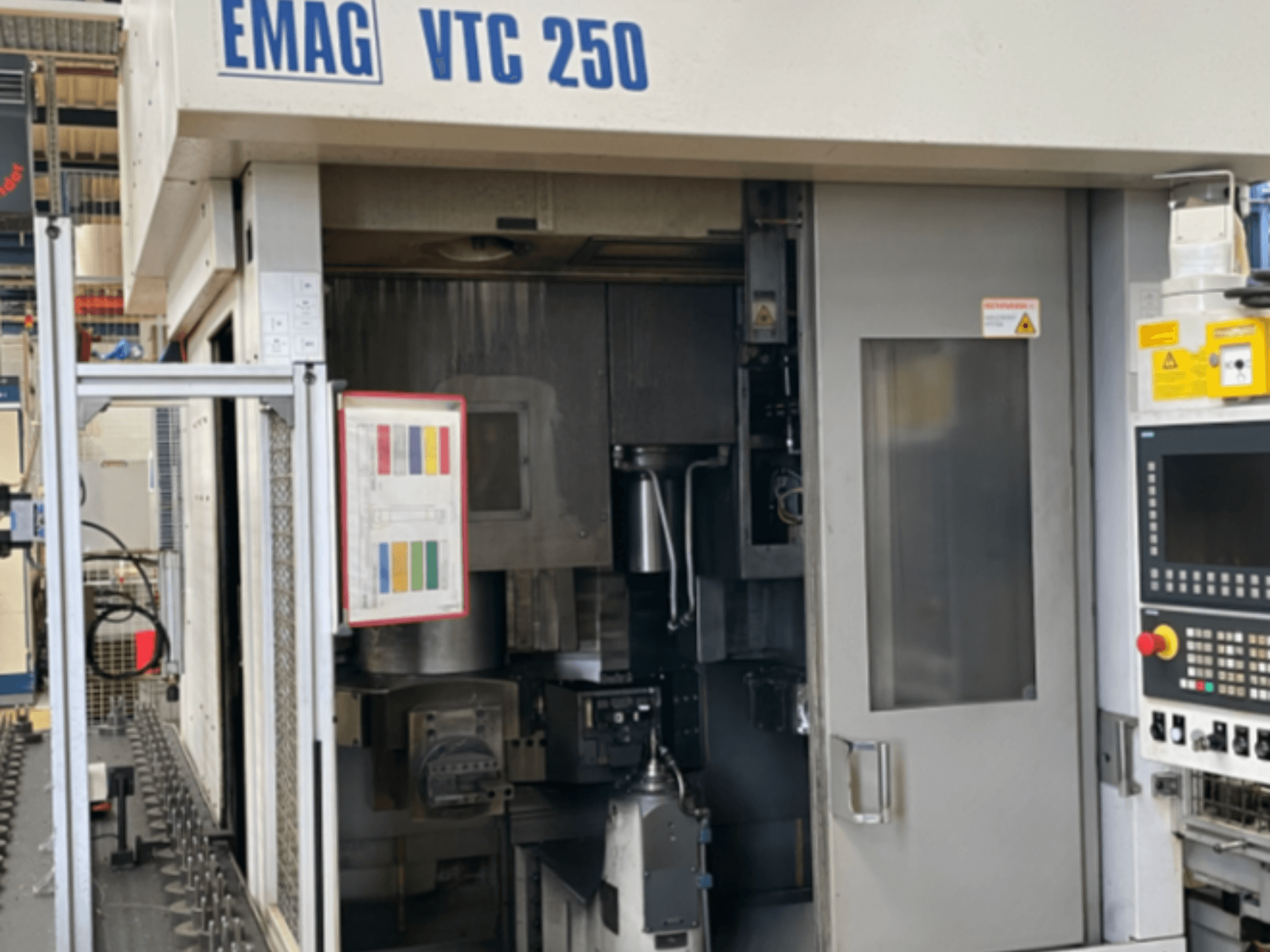 Vista frontal do torno vertical EMAG VTC 250, mostrando o painel de controlo, a interface operacional e a porta de acesso aberta.