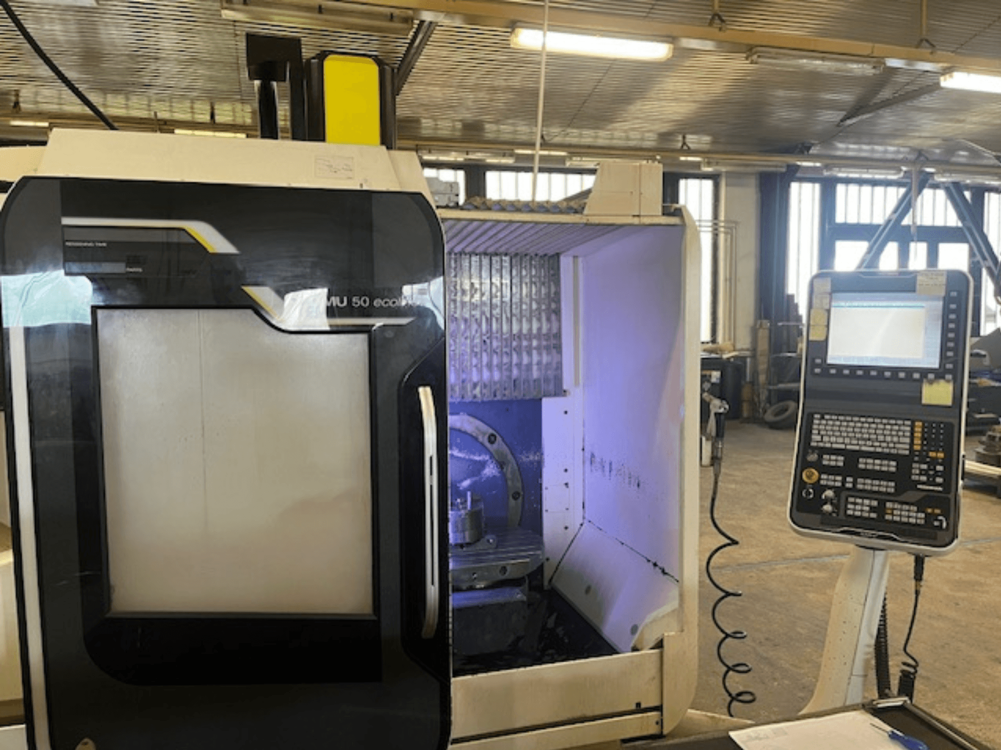 Vista frontal da fresadora DMU 50 eco com painel de controlo, mostrando o porta-ferramentas e o espaço de trabalho.