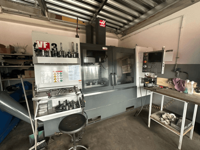 Máquina CNC Haas VF-3 na oficina, vista frontal com ferramentas e controlos na mesa adjacente, apresentando a interface técnica e informações de segurança.