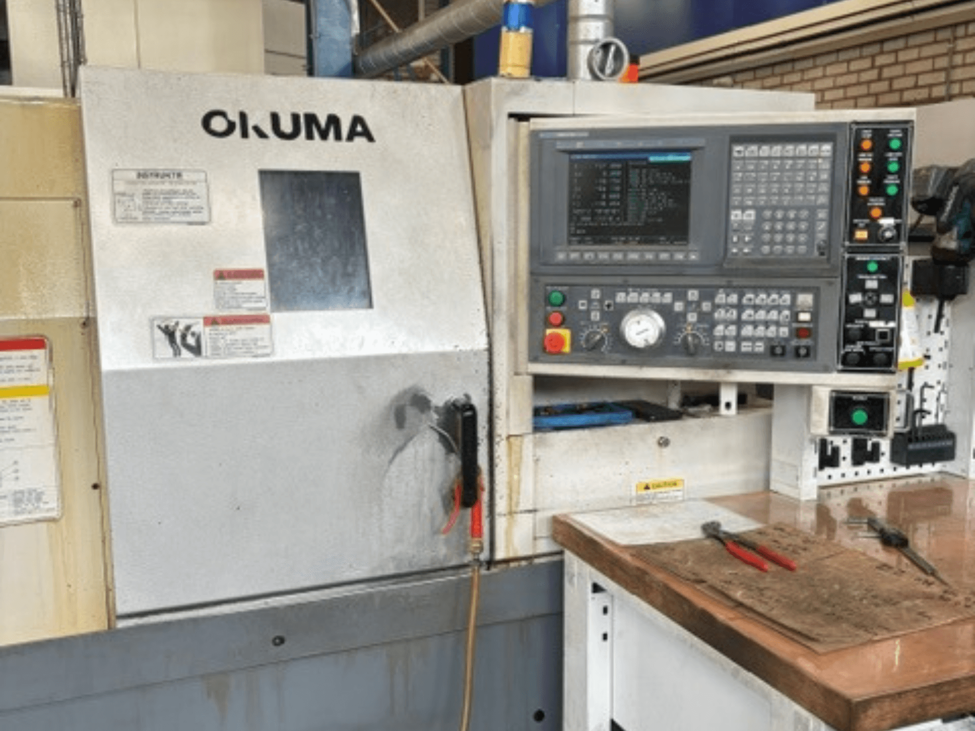 Vista frontal do torno horizontal Okuma ES-L10II, com o painel de controlo, o ecrã e a área de trabalho com ferramentas.