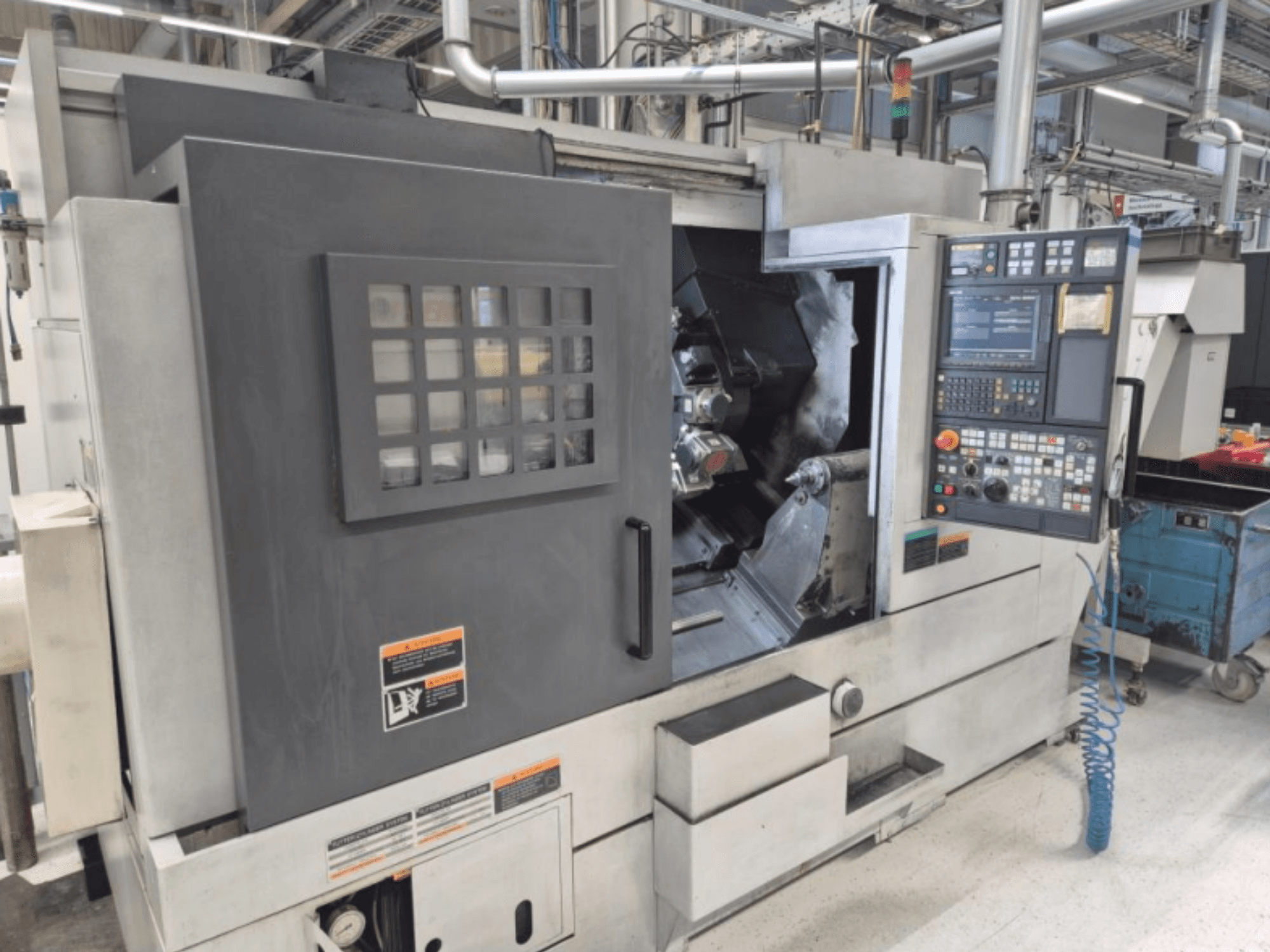 Máquina de torno CNC com painel de controlo, vista frontal. Apresenta uma área de trabalho visível e uma janela de segurança, marca desconhecida.