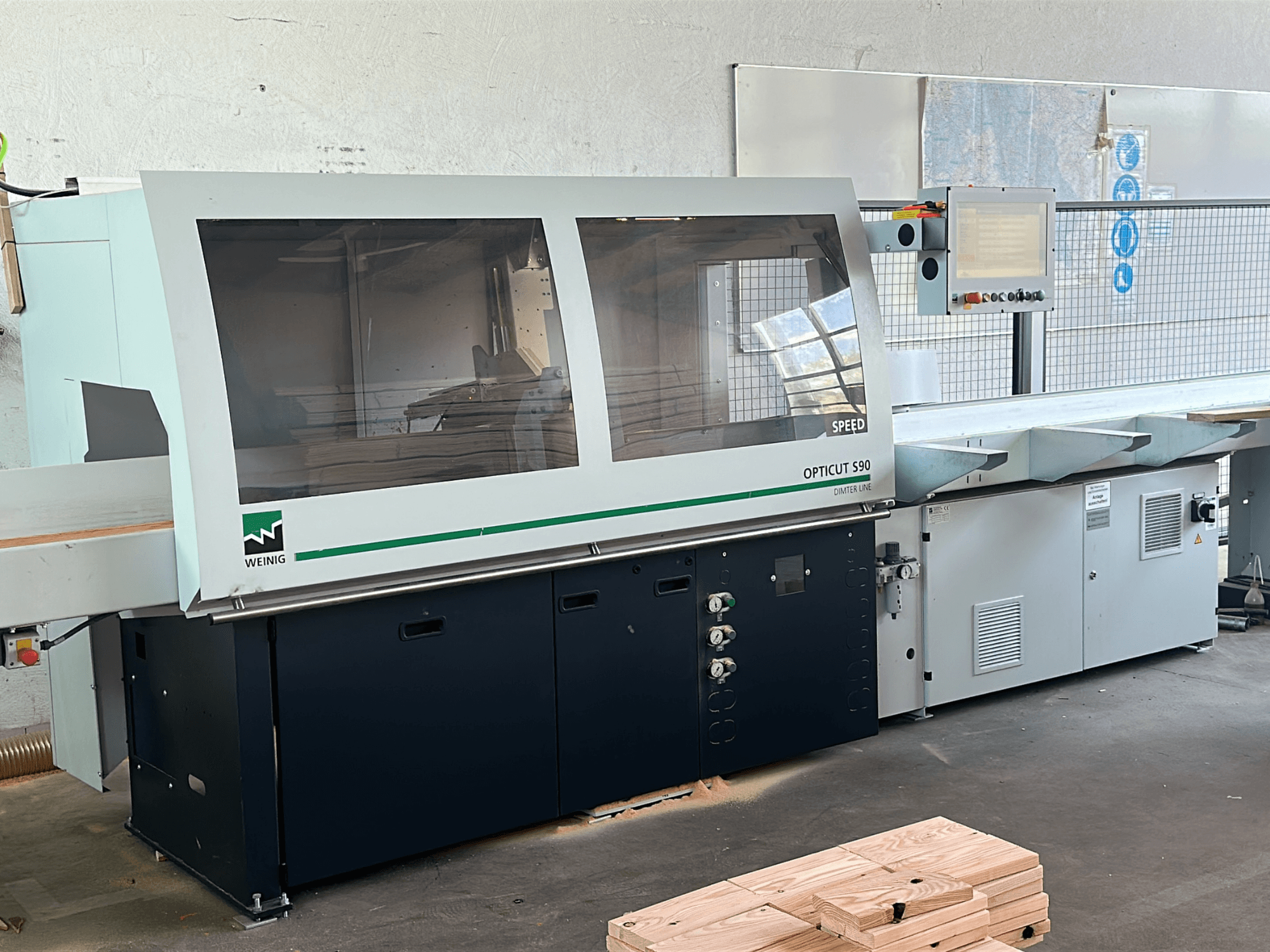 WEINIG Opticut S90, serra de corte transversal optimizada, em vista frontal, com caixa de segurança transparente e painel de controlo.