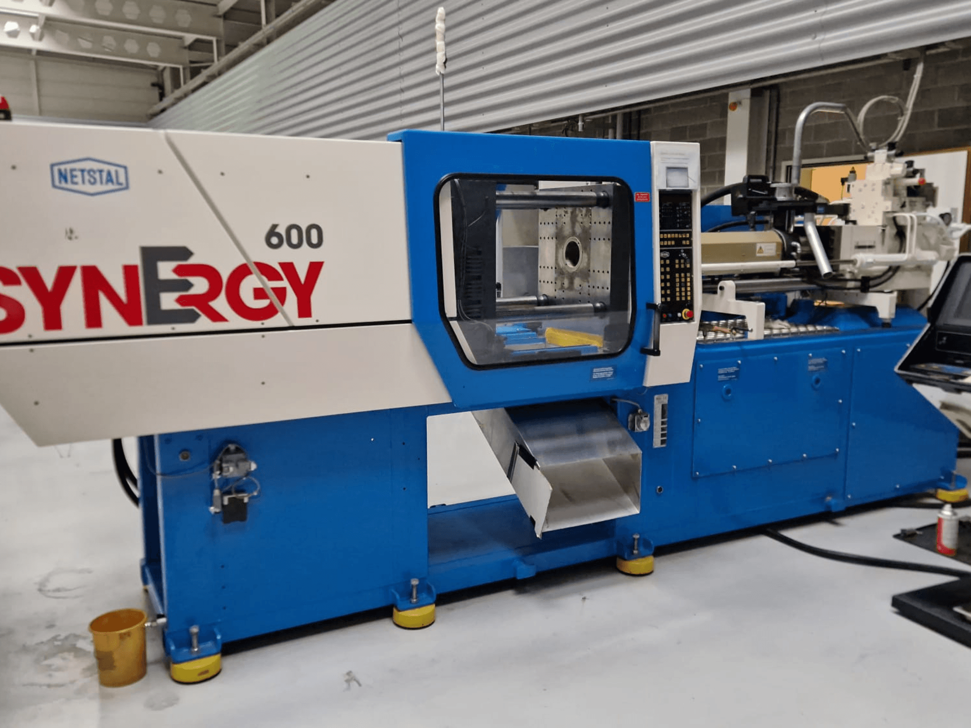 Máquina de moldagem por injeção hidráulica Netstal Synergy 600-230, vista lateral mostrando o painel de controlo e a área de injeção.