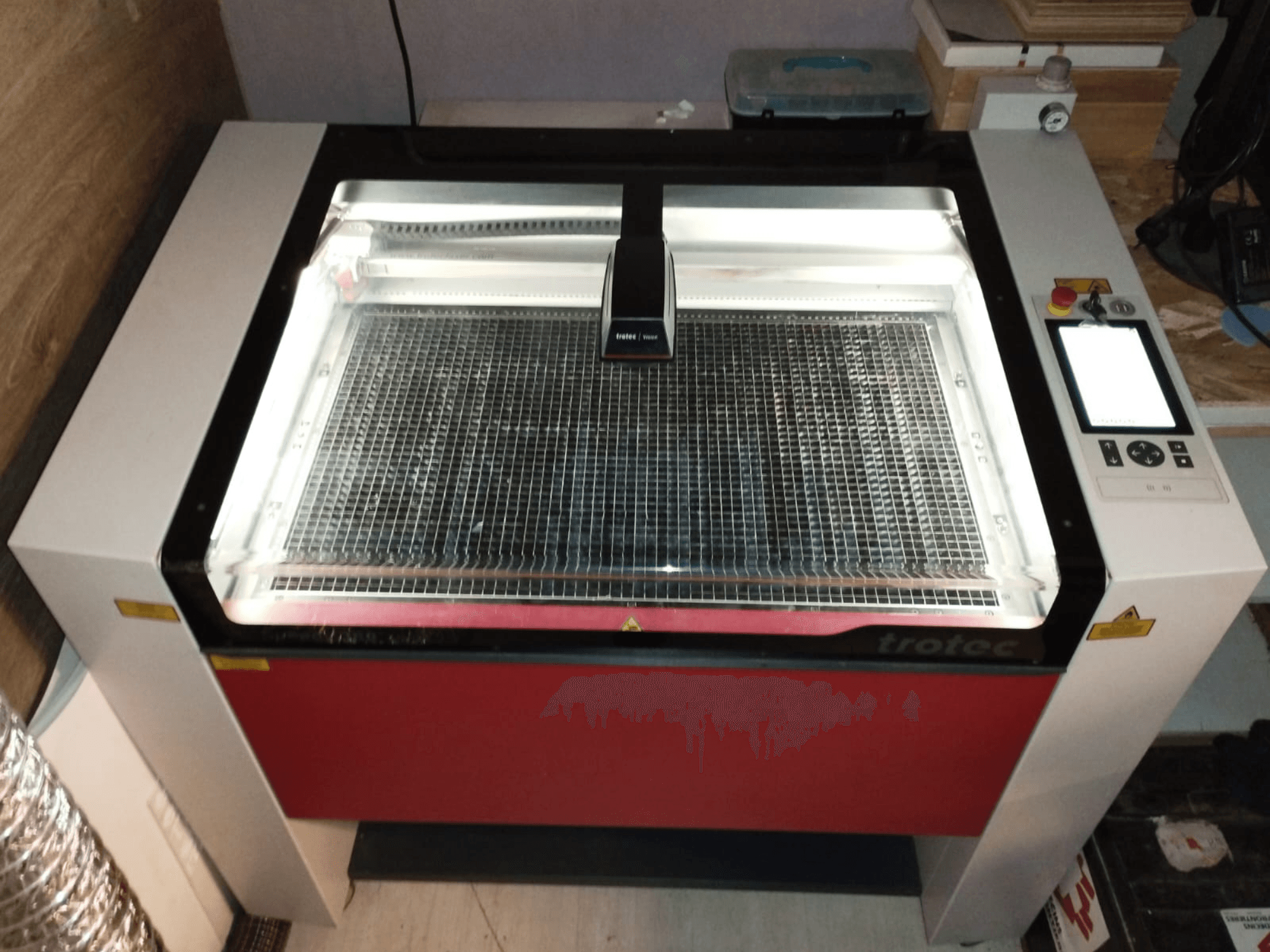 Cortador laser Trotec com uma tampa transparente, base de grelha e painel de controlo à direita; vista frontal mostrando o design e as caraterísticas.