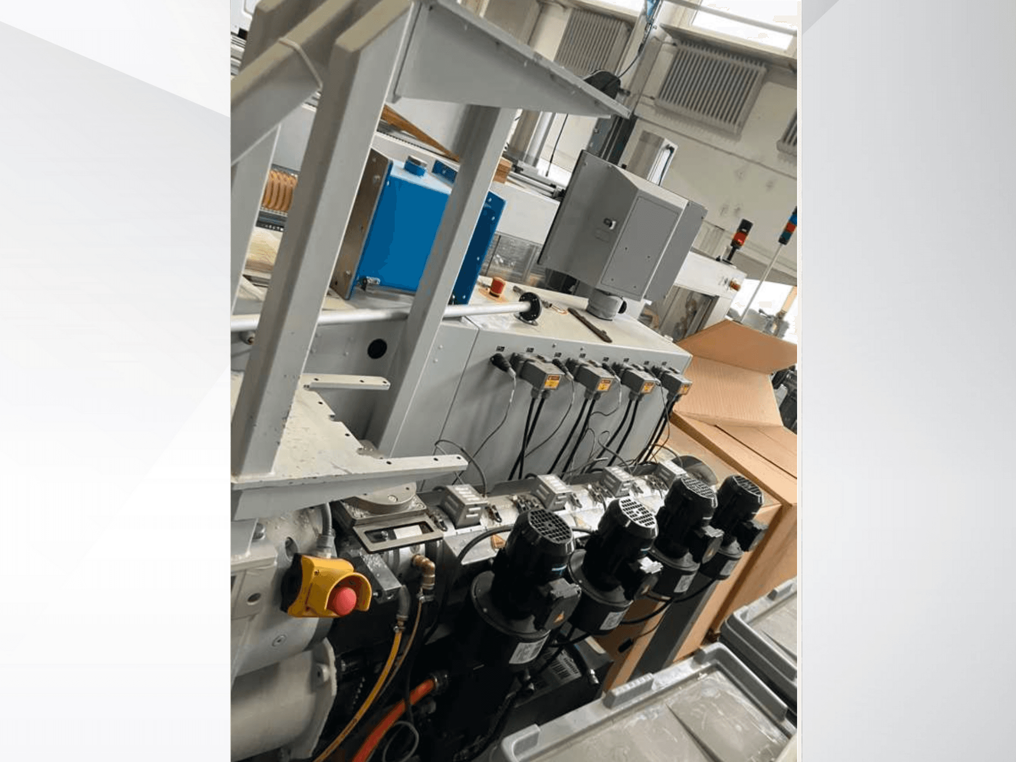 Painel de controlo de máquinas industriais com vários motores, manómetros e um monitor; vista lateral no interior de uma fábrica.