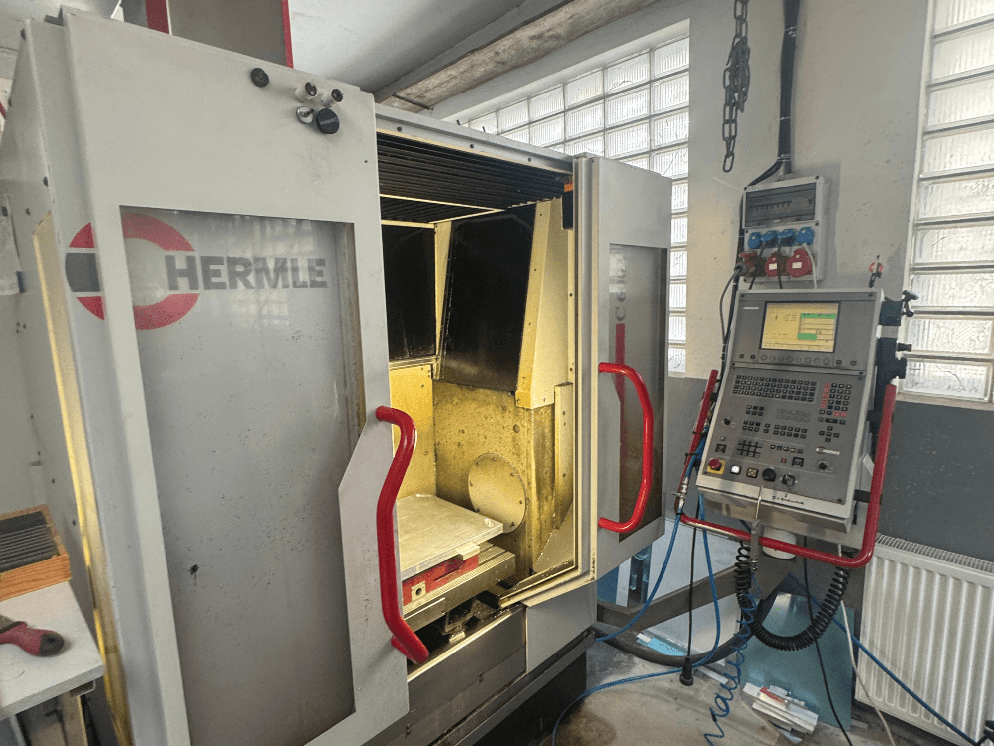Centro de maquinação vertical HERMLE C600V, vista frontal mostrando a porta aberta, o painel de controlo e a área de trabalho interior.