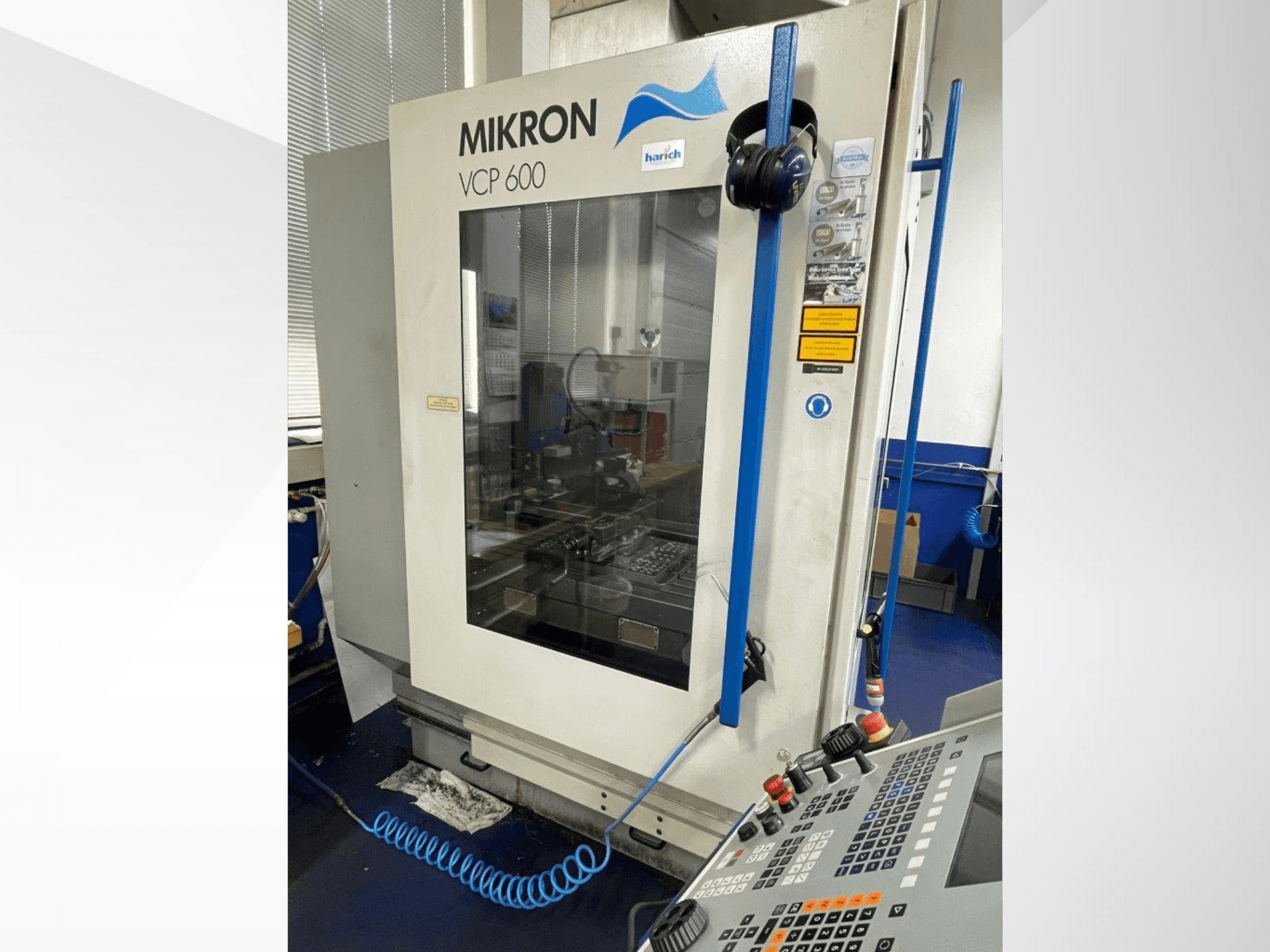 Máquina CNC Mikron VCP 600, vista frontal, com painel de controlo com botões e área de maquinação visível atrás do vidro.