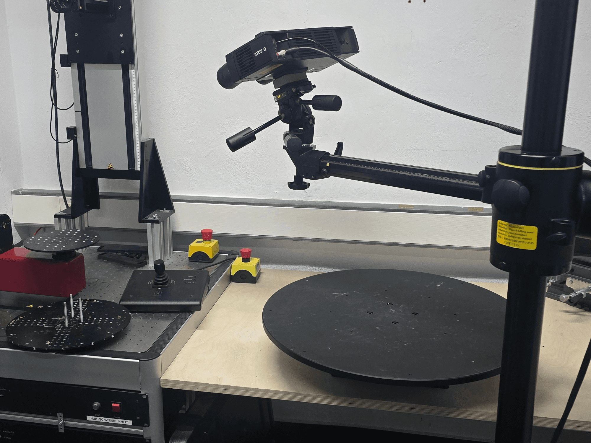 Vista frontal da máquina de medição ótica ZEISS ATOS Q 12M, com uma cabeça de varredura, um painel de controlo e uma plataforma circular rotativa.