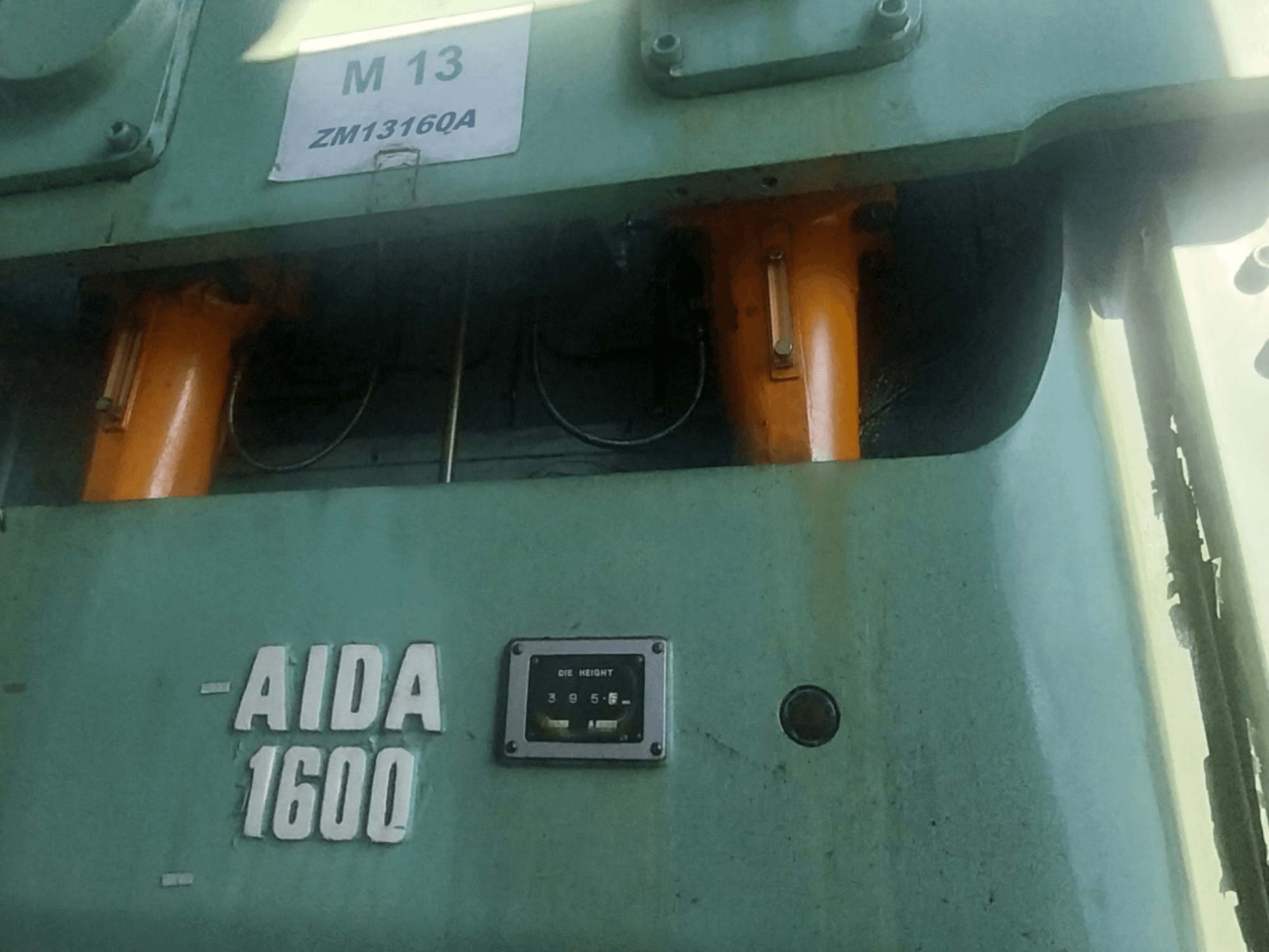 Prensa de estampagem mecânica AIDA NC2-1600, vista frontal; componentes hidráulicos laranja e medidor de altura da matriz visíveis.