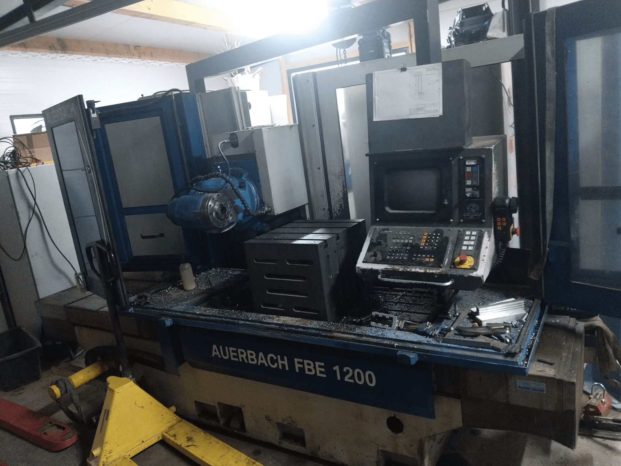 Máquina de perfuração de metal Auerbach FBE 1200, vista frontal, mostrando o painel de controlo, motor e aparas de metal na superfície de trabalho.