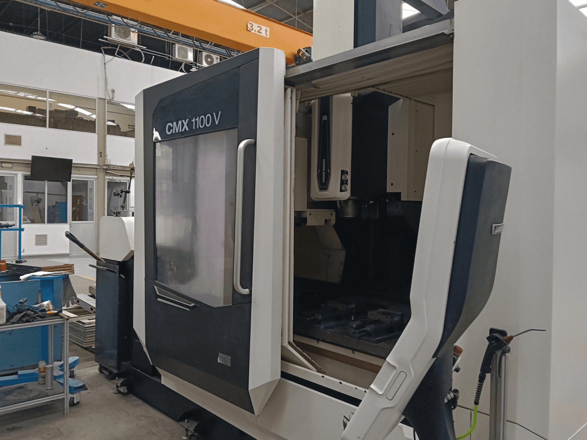 Centro de maquinagem vertical DMG MORI CMX 1100 V, vista frontal que mostra a porta aberta e a configuração das ferramentas no interior, num espaço industrial.