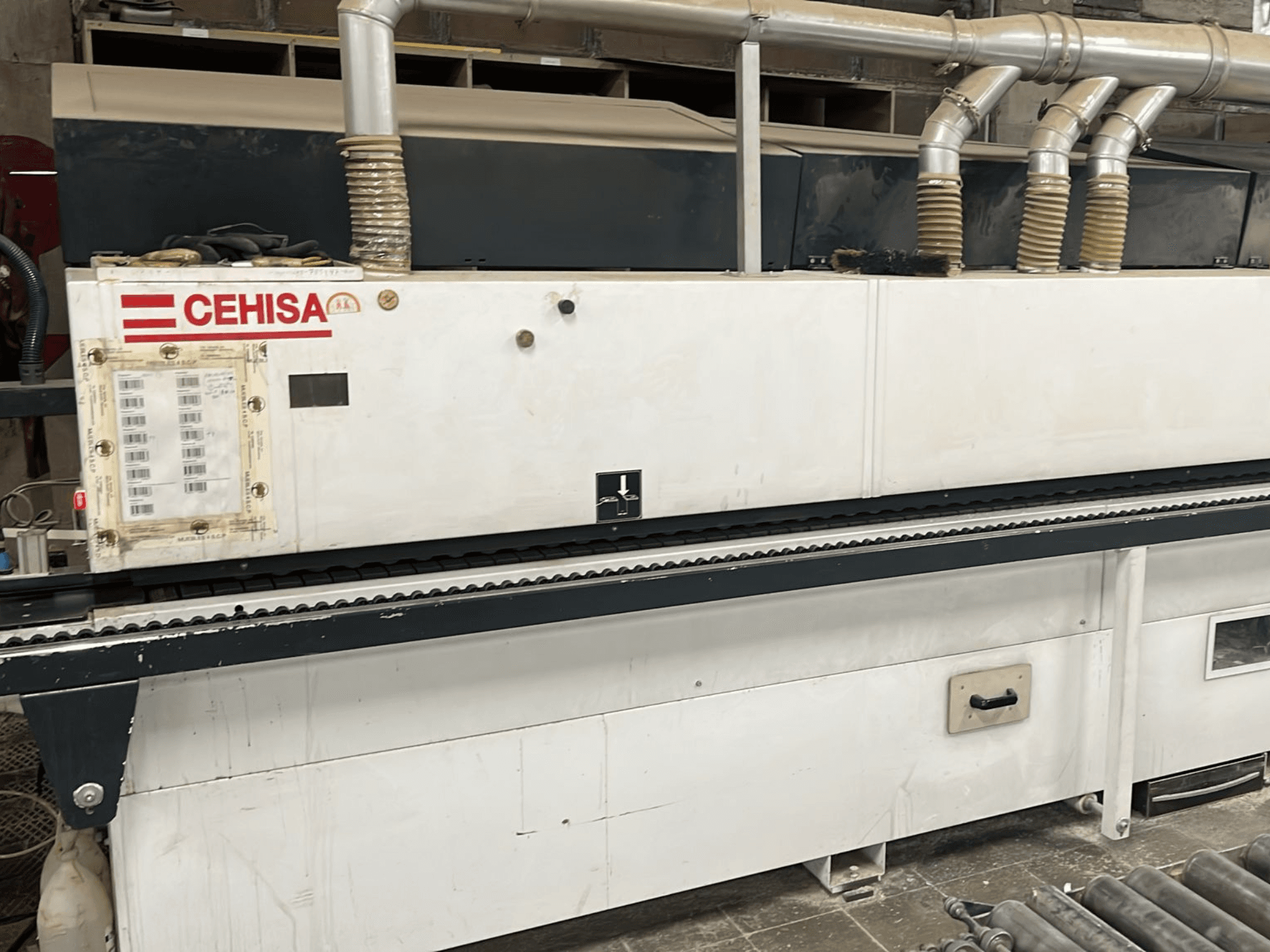 Máquina de encolagem de bordas CEHISA PRO 12 CONCEPT vista de frente, com o painel de controlo, os tubos de extração de pó e a correia transportadora.
