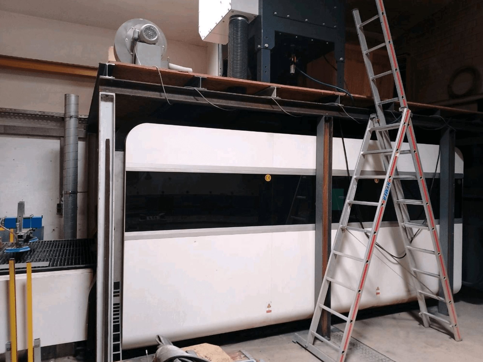Máquina de corte a laser de fibra GWEIKE LF3015GA numa oficina, mostrando a vista frontal, a estrutura metálica e a escada de acesso.