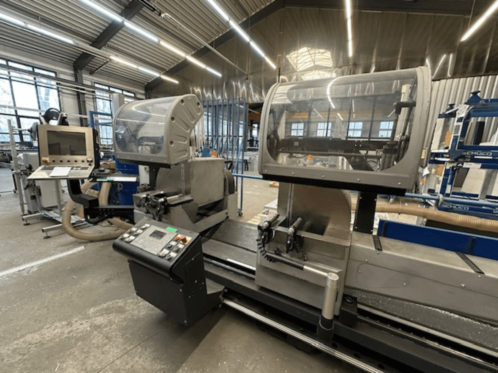 Serra circular para metal SCHÜCO PDG E CUT, vista frontal, com painel de controlo, coberturas de proteção e área de corte numa oficina.