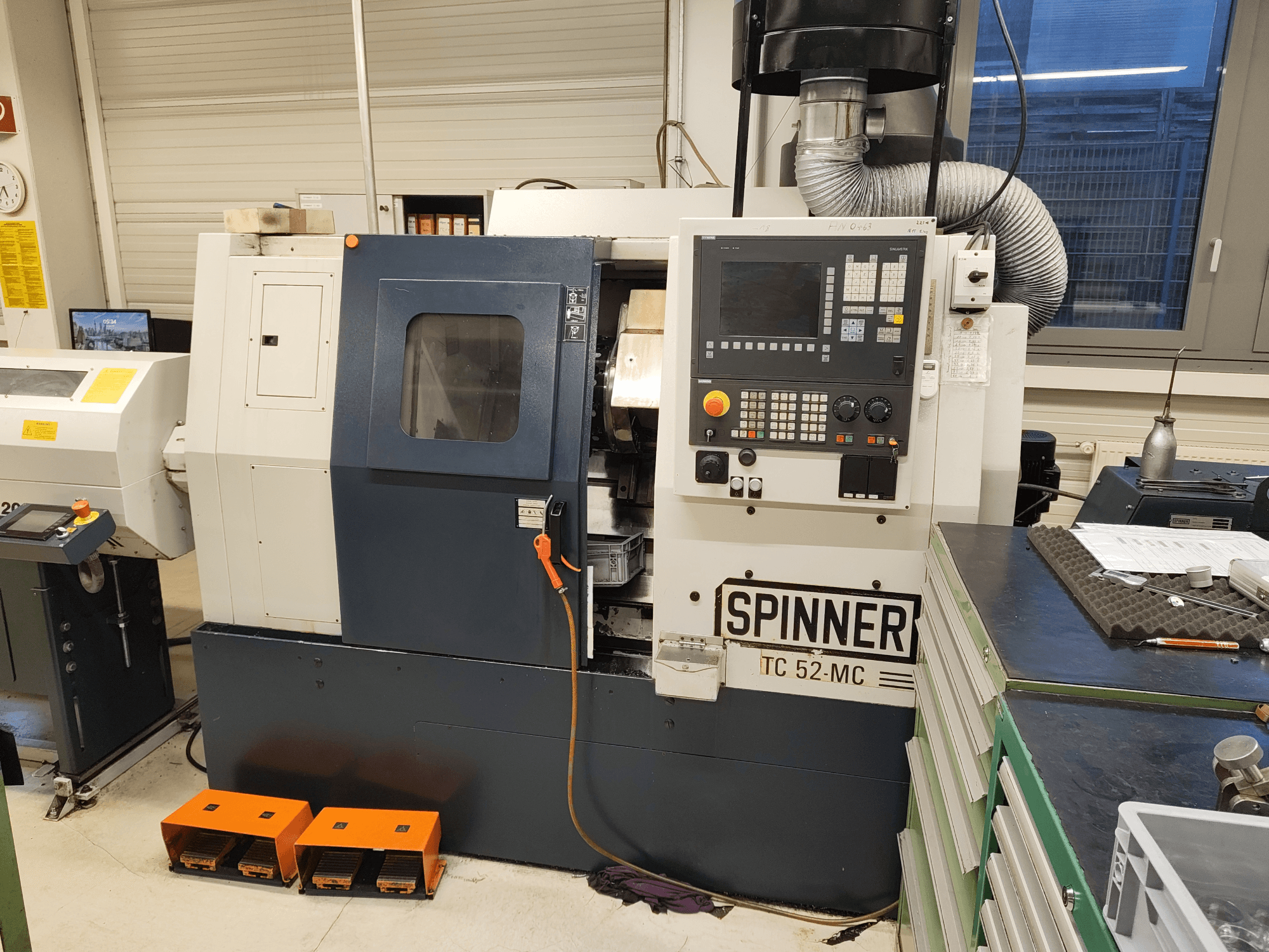 Torno horizontal SPINNER TC 52 MC numa oficina, vista frontal, mostrando o painel de controlo, a área de maquinagem e os dispositivos de segurança.