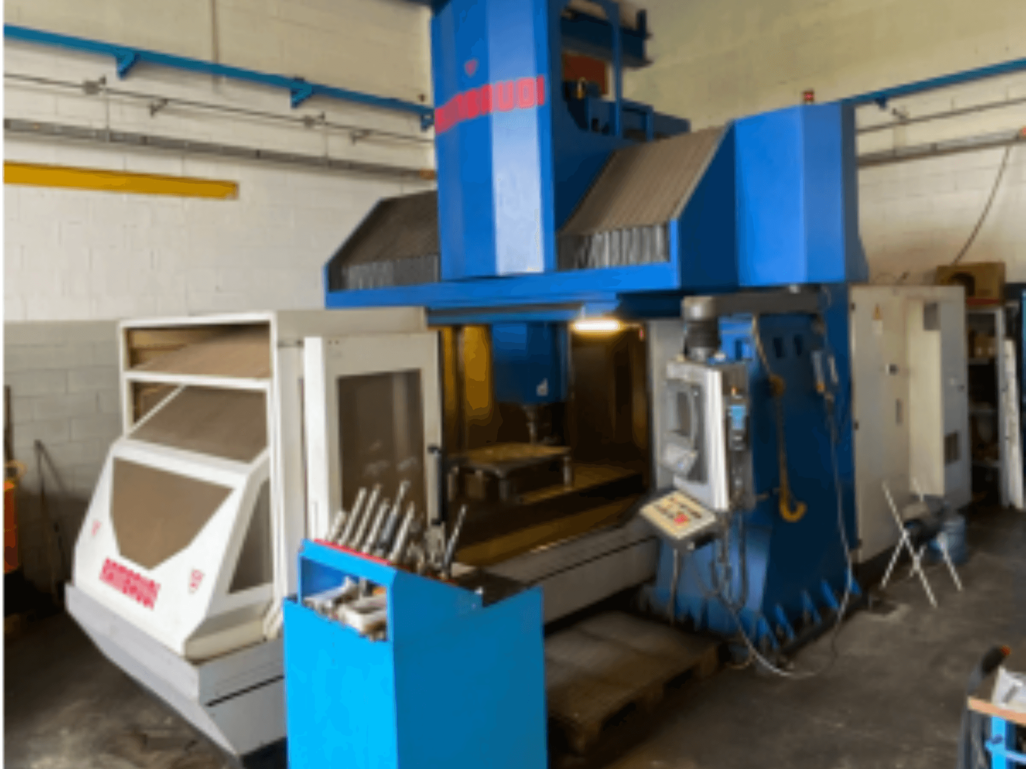 Centro de maquinação vertical Rambaudi RF103, vista frontal mostrando controlos, armazenamento de ferramentas e área de maquinação. Exterior azul e branco.