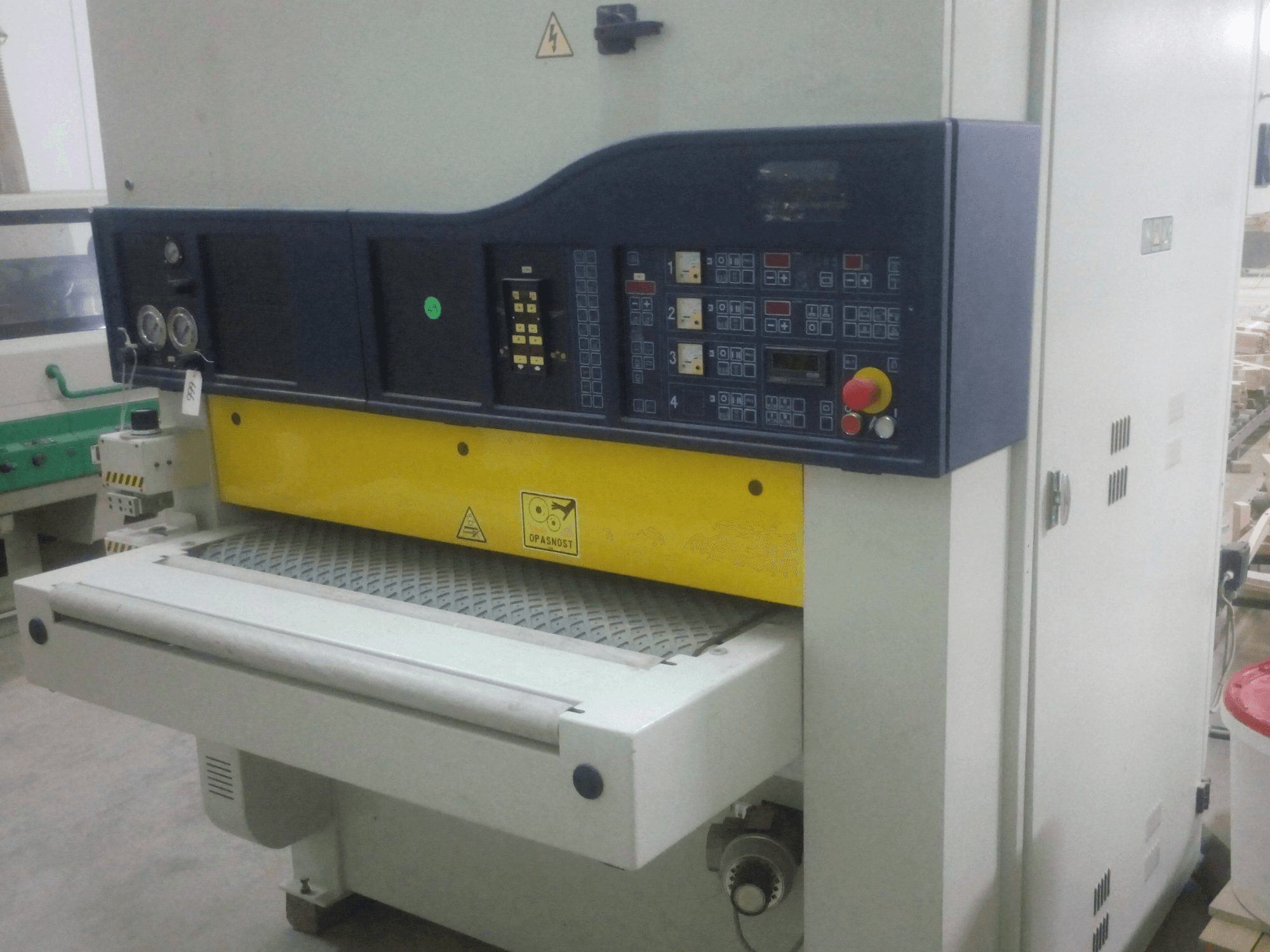 Máquina de lixar industrial com painel de controlo, corpo amarelo e azul, vista frontal, mostrando indicadores, interruptores e superfície de transporte.