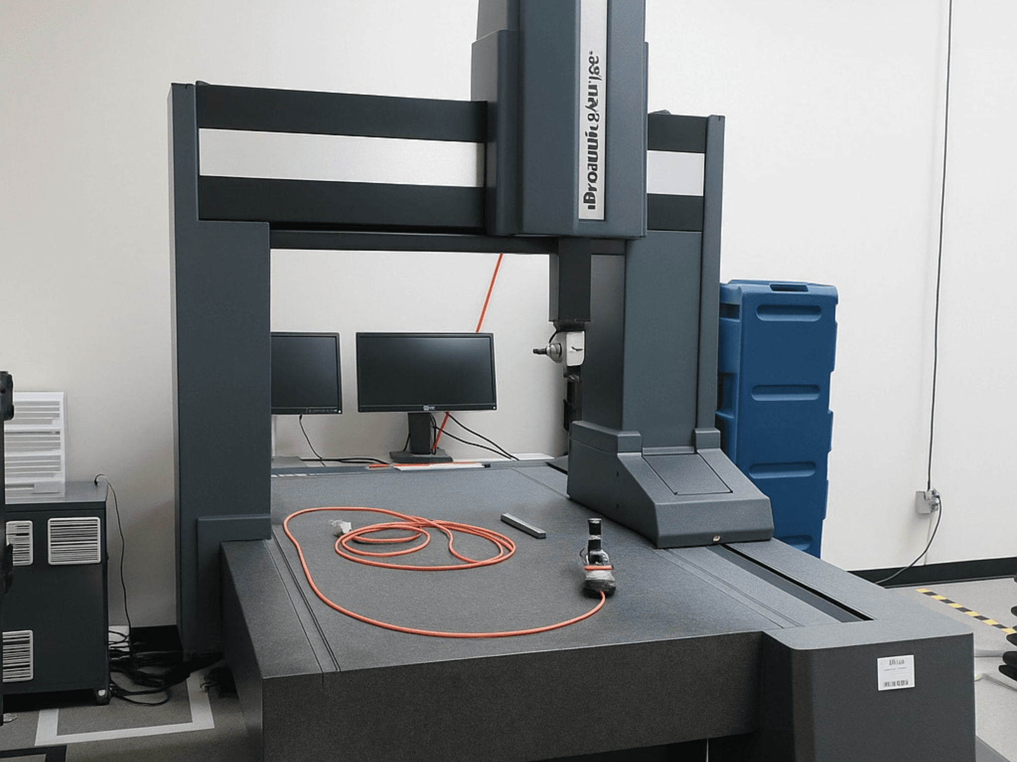 Máquina de medição por coordenadas da Brooks Automation com dois monitores, vista frontal, com um tampo de mesa cinzento e ferramentas de medição.