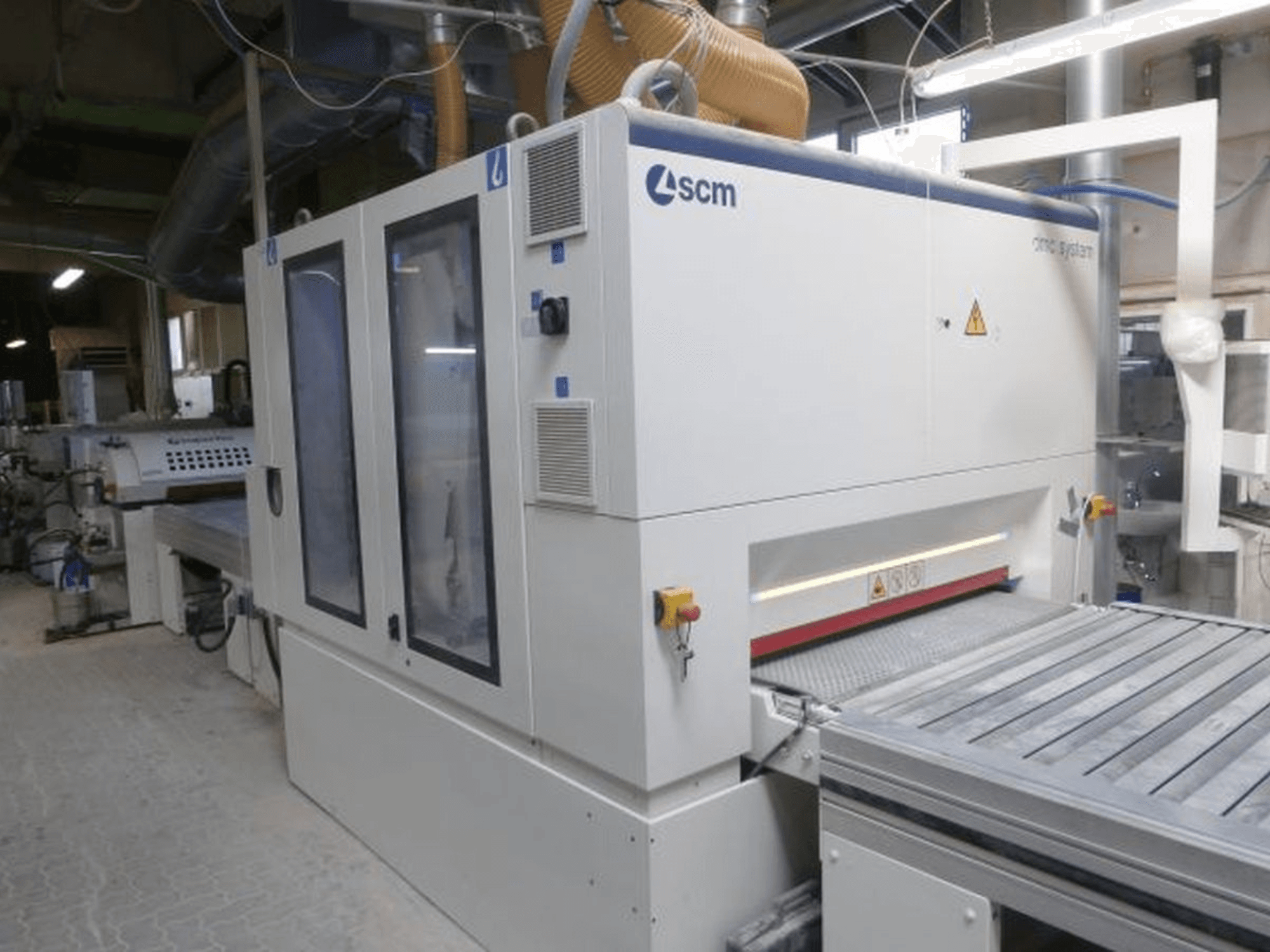 Lixadeira de cinta SCM DMC SY TC 1350 numa oficina, vista lateral que mostra o painel de controlo e a superfície de lixagem com dispositivos de segurança.