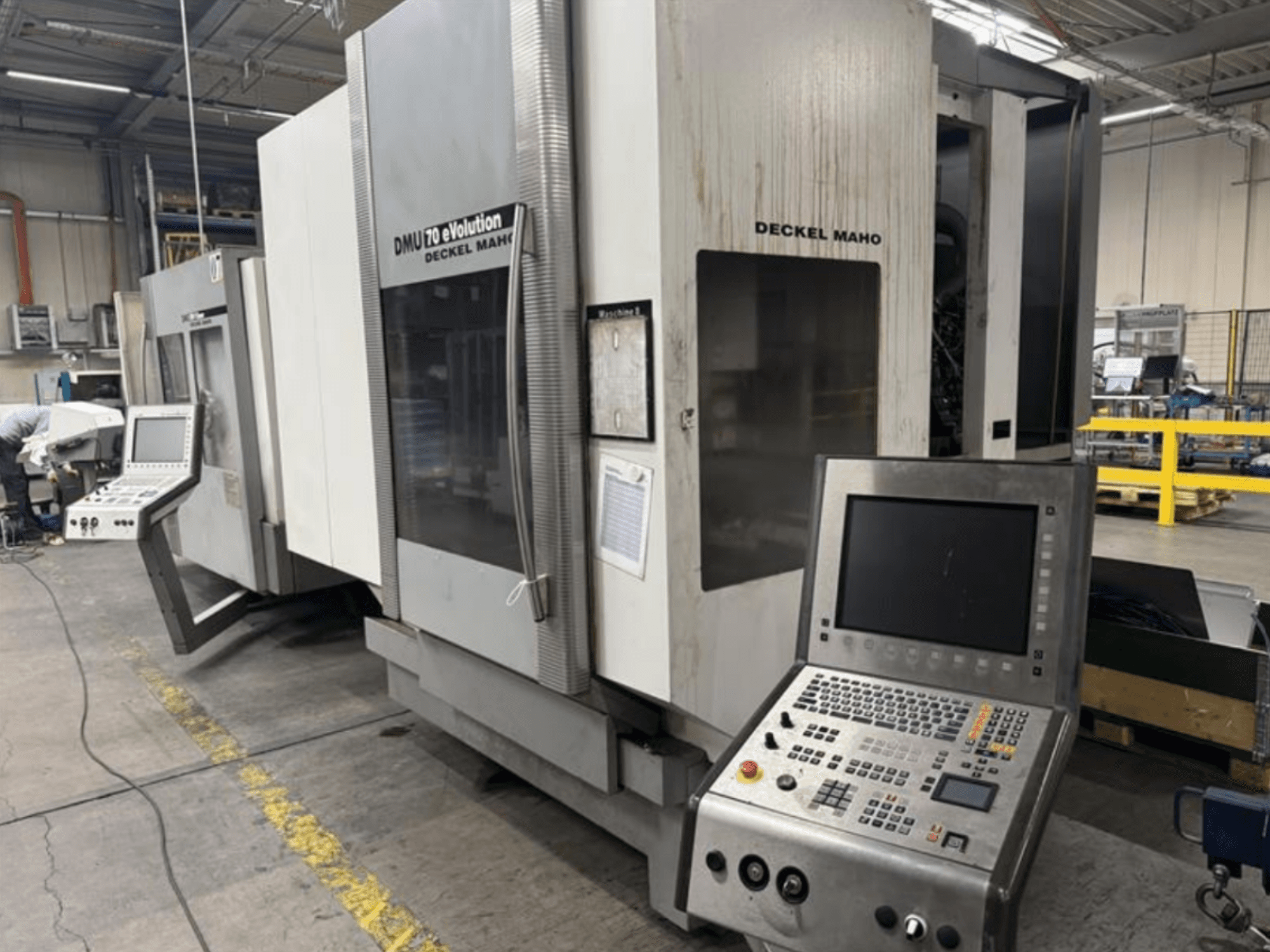 Vista frontal de uma máquina CNC Deckel Maho DMU 70 eVOLUTION com painel de controlo, localizada numa instalação de fabrico.