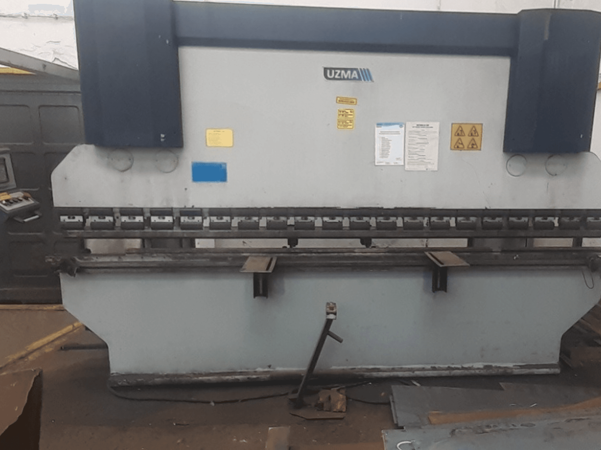 Prensa dobradeira UZMA HAP 40160 em vista frontal, com controlos, avisos de segurança e ferramentas de dobragem de metal.