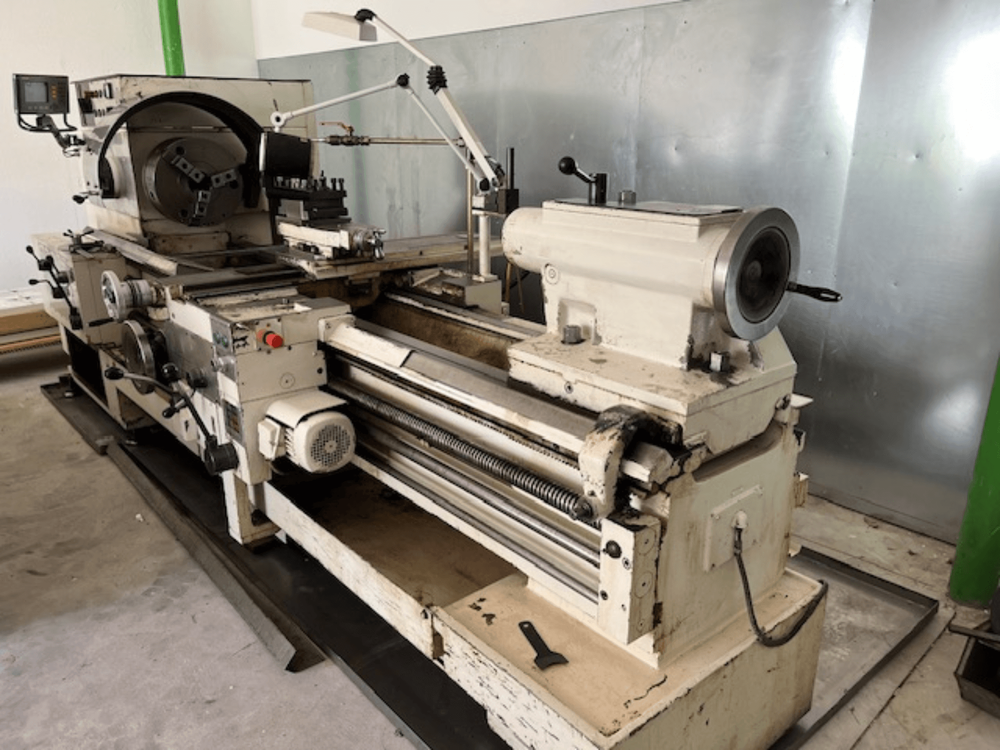 Torno metálico vintage com painel de controlo e ferramentas, vista lateral, mostrando elementos operacionais e acabamento metálico.
