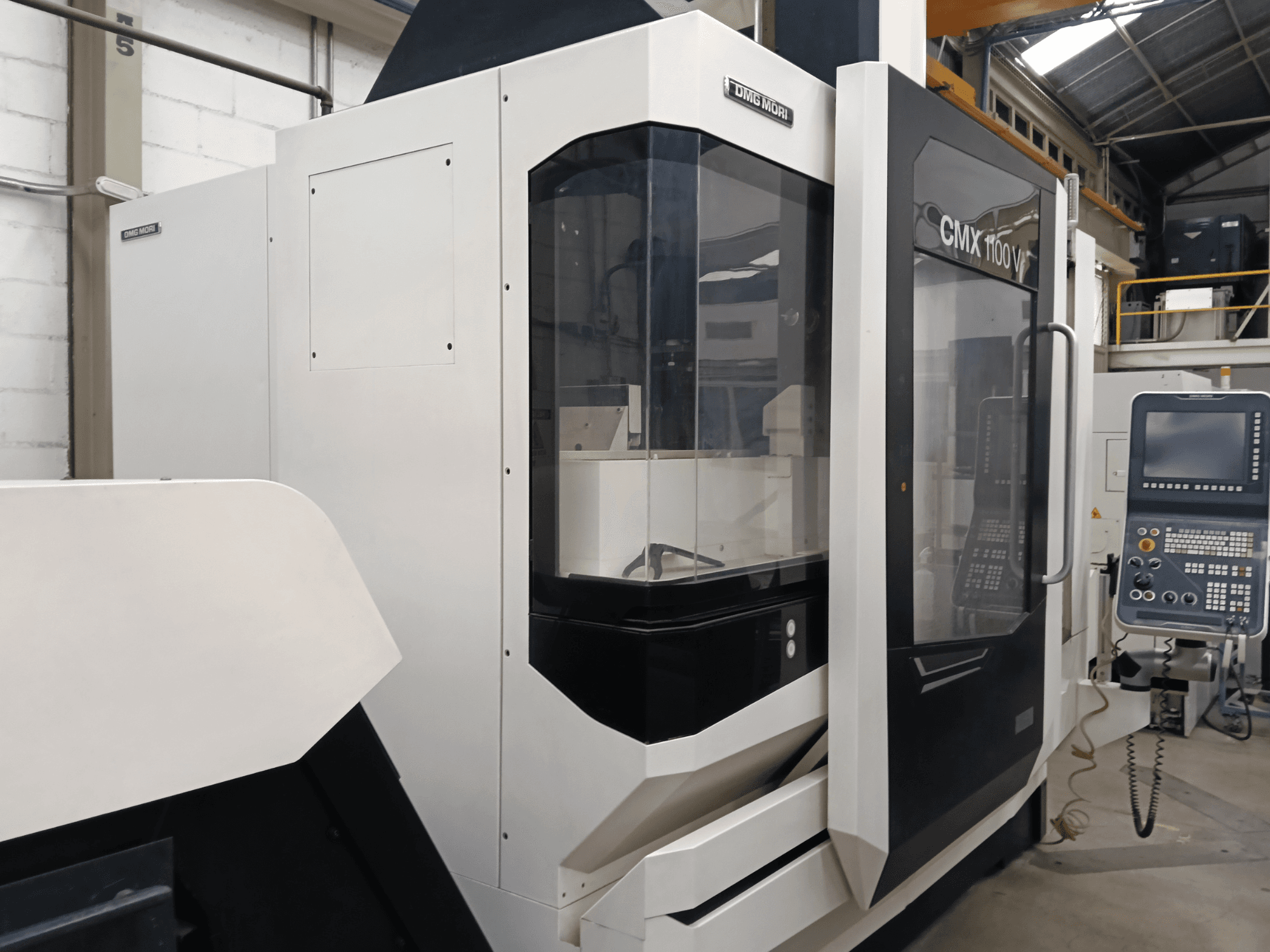 Centro de maquinagem vertical DMG MORI CMX 1100 V, vista frontal, mostrando o painel de controlo e a cobertura de vidro.