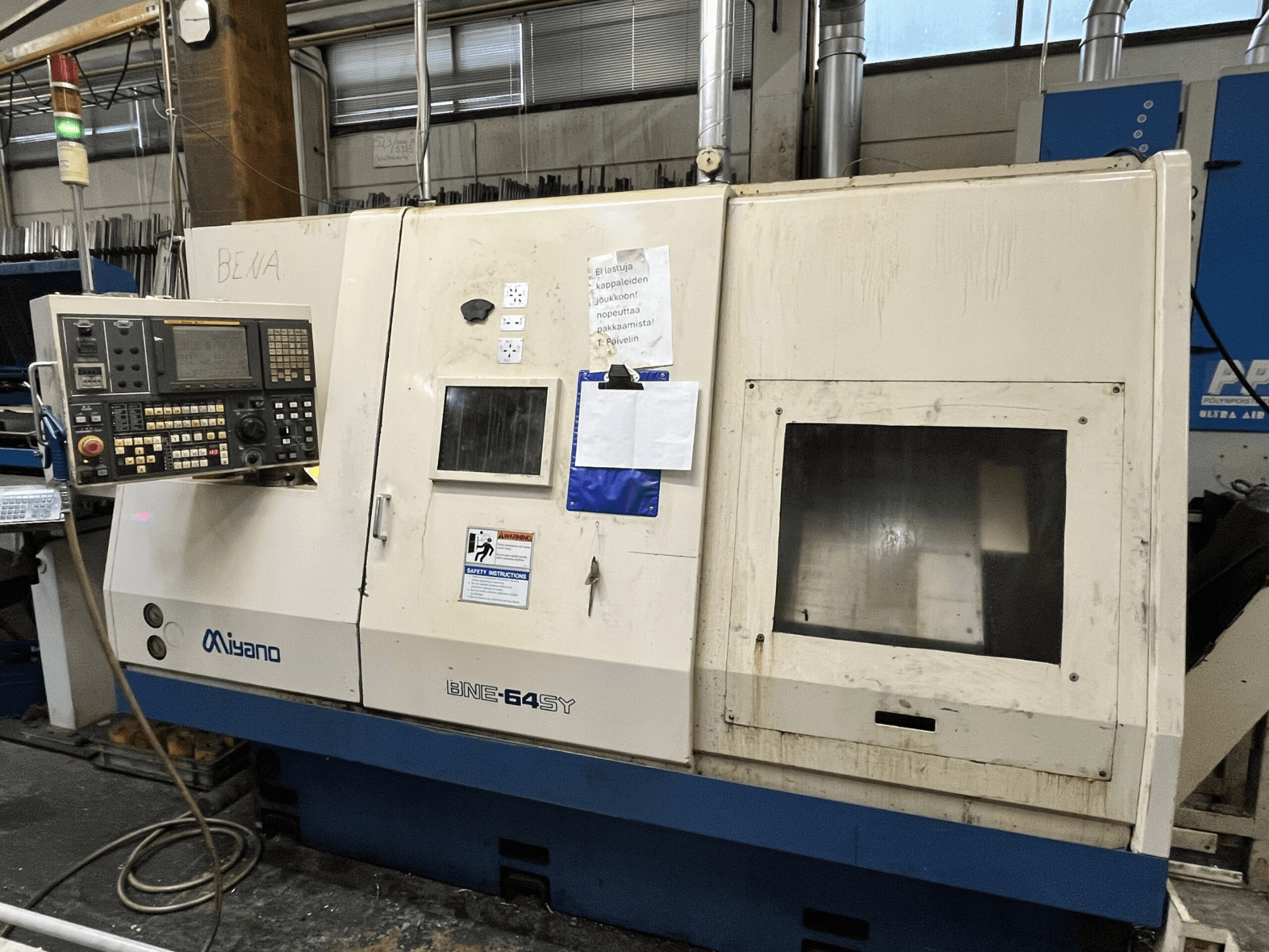 Torno CNC Miyano BNE-64SY, vista frontal, com painel de controlo com botões, LCD e autocolantes de manutenção no armário.