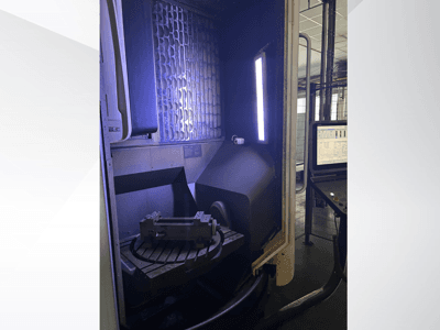 Centro de maquinagem vertical DMG MORI DMU 65 MonoBlock, vista frontal que mostra a mesa rotativa com a peça de trabalho e o painel de controlo.