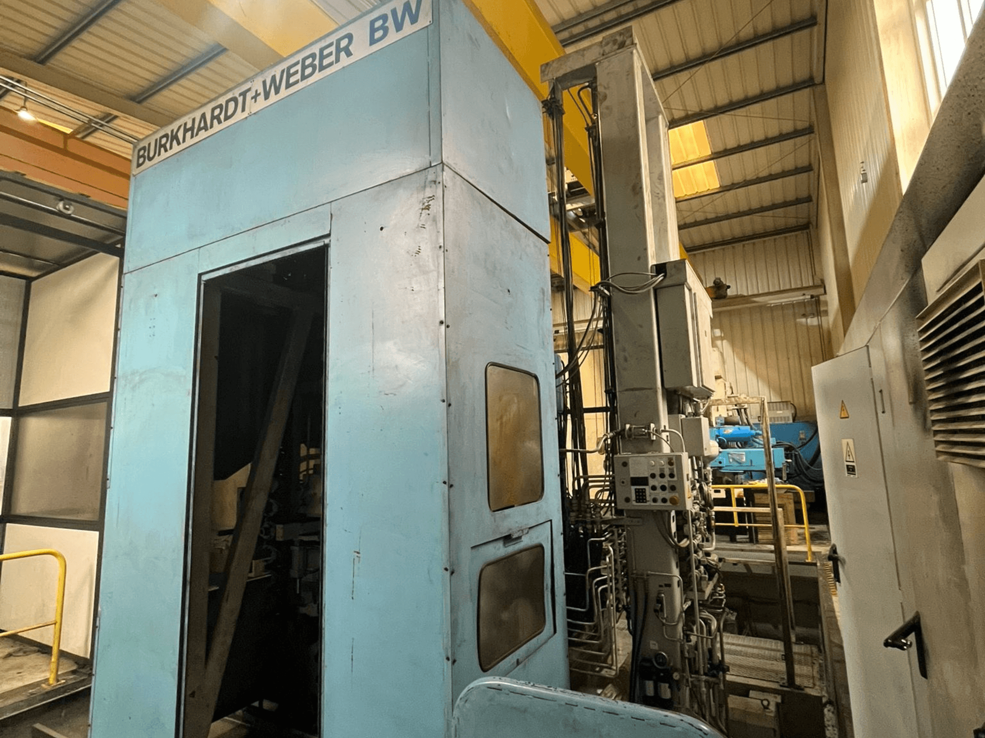 Centro de maquinagem horizontal Burkhardt-Weber MC100, vista lateral que mostra o exterior azul e o painel de controlo com a tubagem visível.