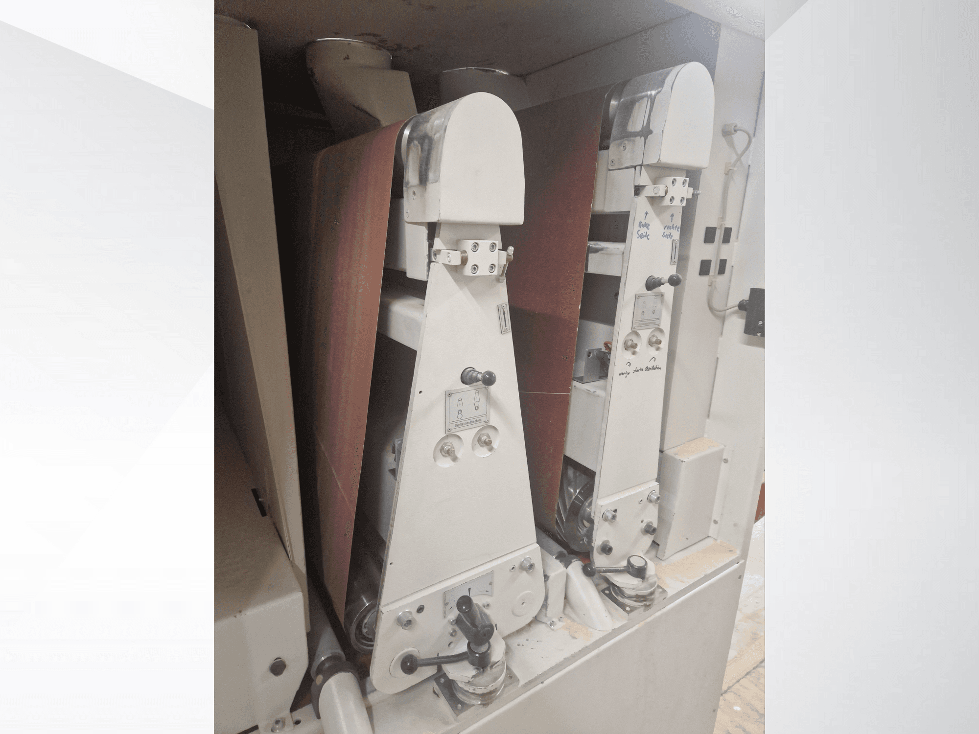 Duas máquinas de lixar industriais com cintas de lixa vermelhas, vista frontal, mostrando os controlos e os componentes metálicos.