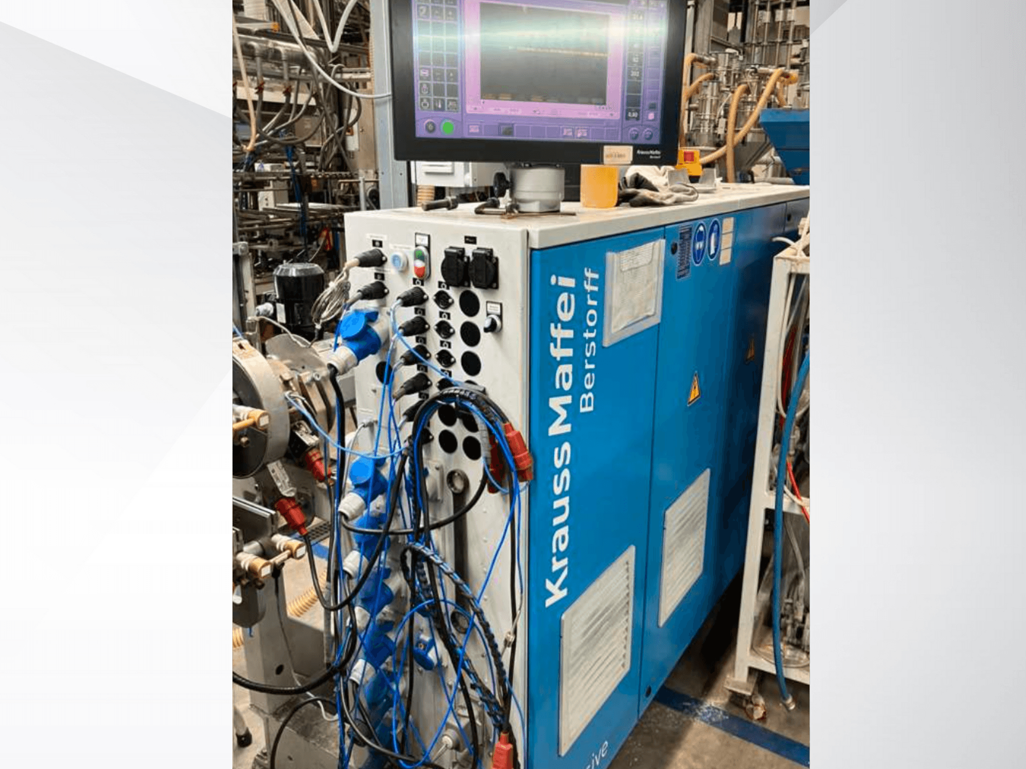 Máquina industrial Krauss Maffei Berstorff com painel de controlo e monitor, com vários botões e mangueiras ligadas, vista lateral.