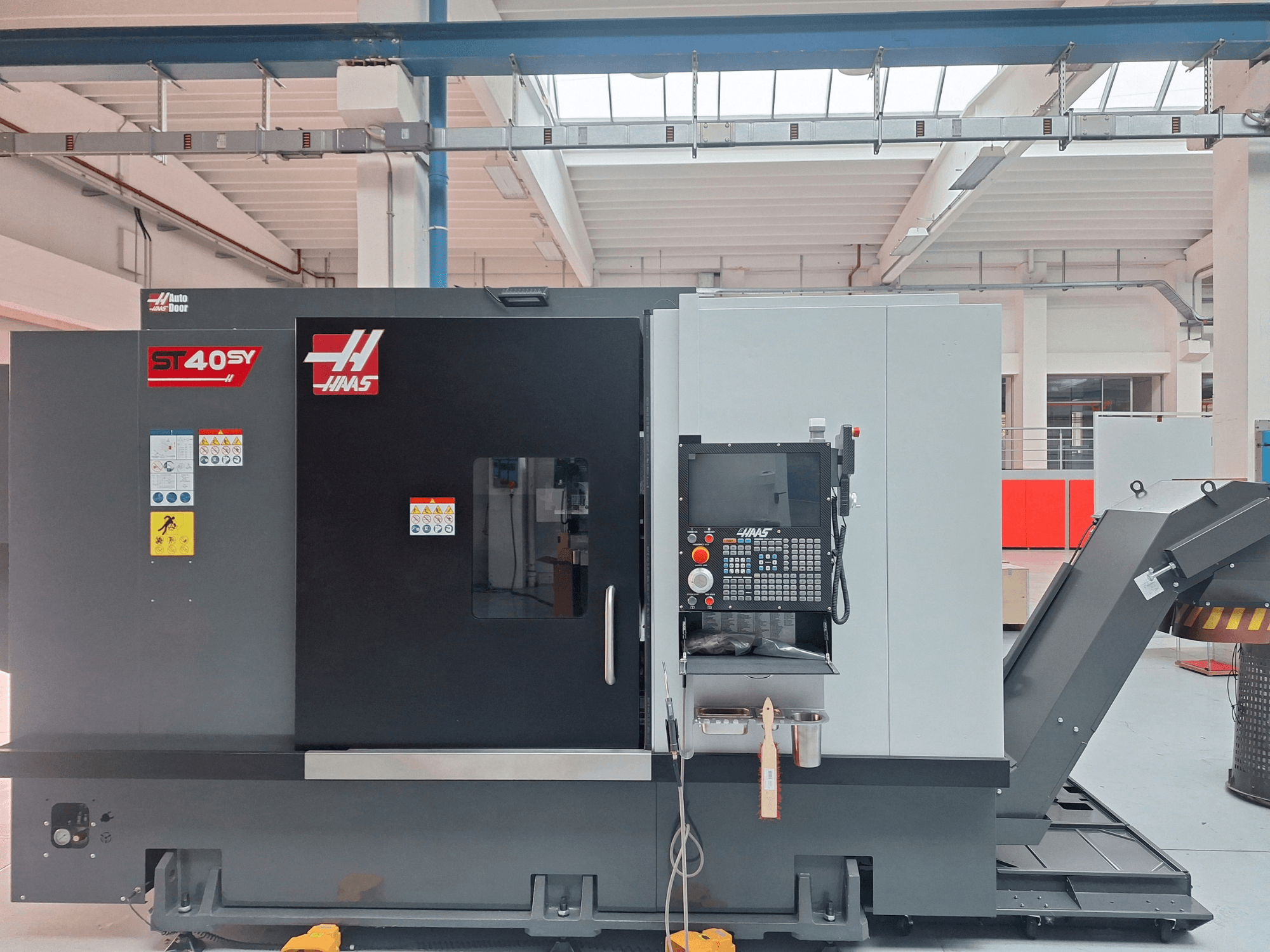 Torno horizontal Haas ST-40SY numa vista lateral, apresentando um painel de controlo e etiquetas de segurança.