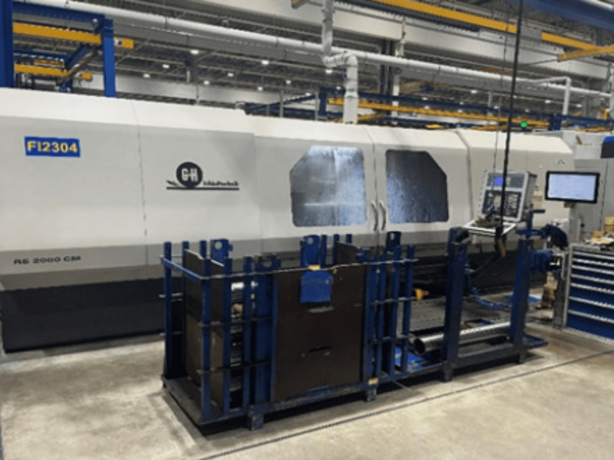 Máquina CNC GH RS 2000 CM numa configuração de fábrica, vista de lado, com painel de controlo e suporte da peça de trabalho.