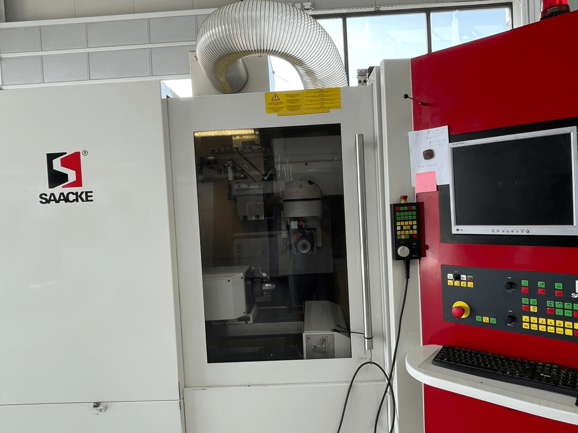 Máquina SAACKE em branco e vermelho, vista frontal, com painel de controlo, monitor e partes internas visíveis através de vidro.