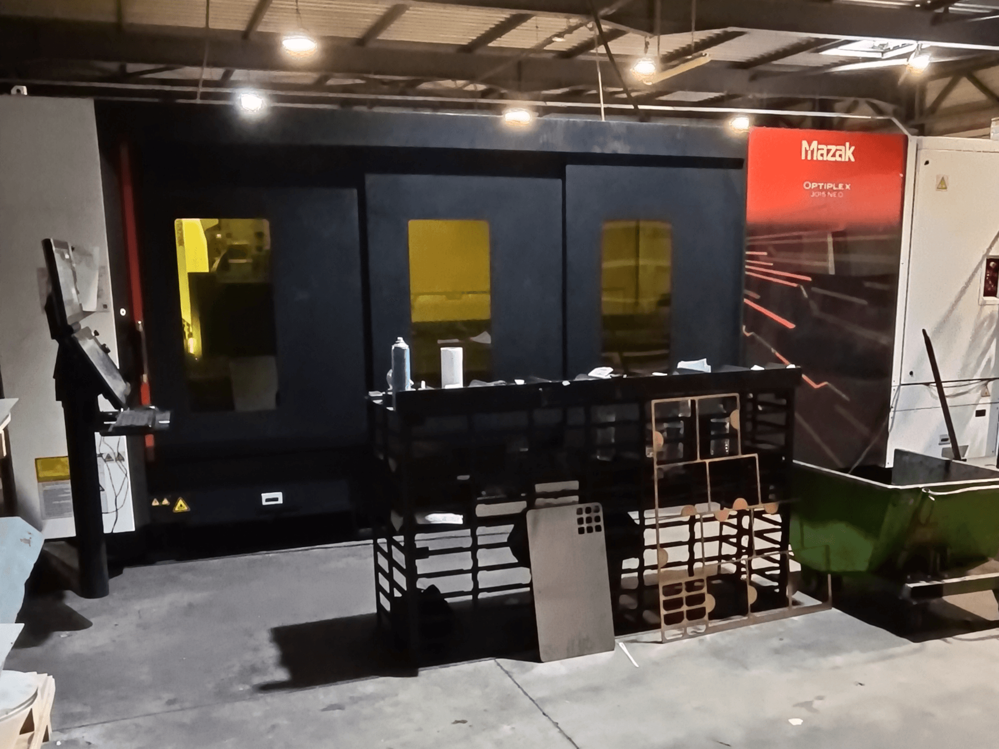 Máquina de corte a laser de fibra Mazak OPTIPLEX NEO numa oficina, vista frontal com o painel de controlo e a área de processamento visíveis.