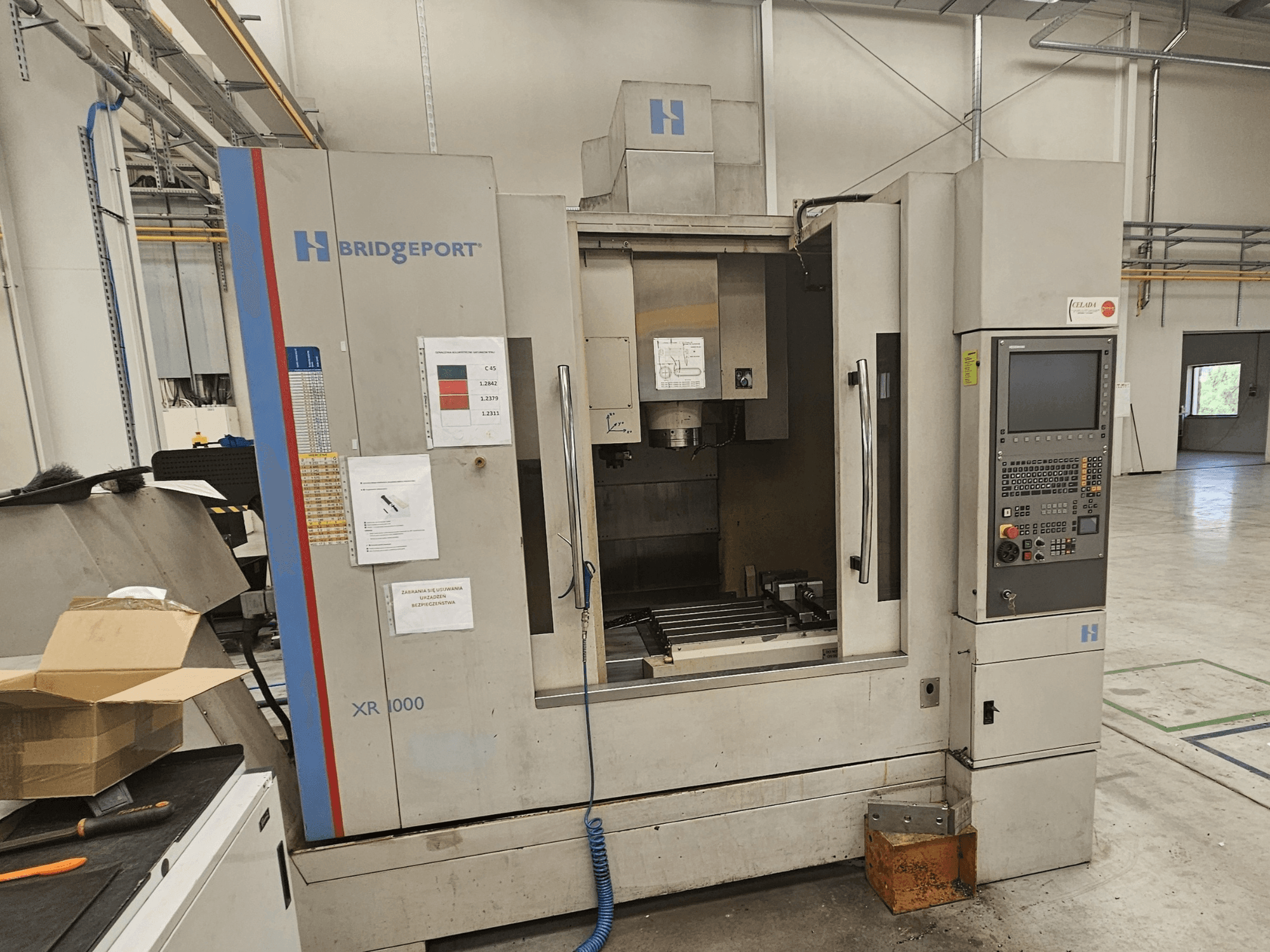 Centro de maquinação vertical Bridgeport XR 1000, vista frontal, com um painel de controlo e uma área de trabalho visível com uma mesa de corte.
