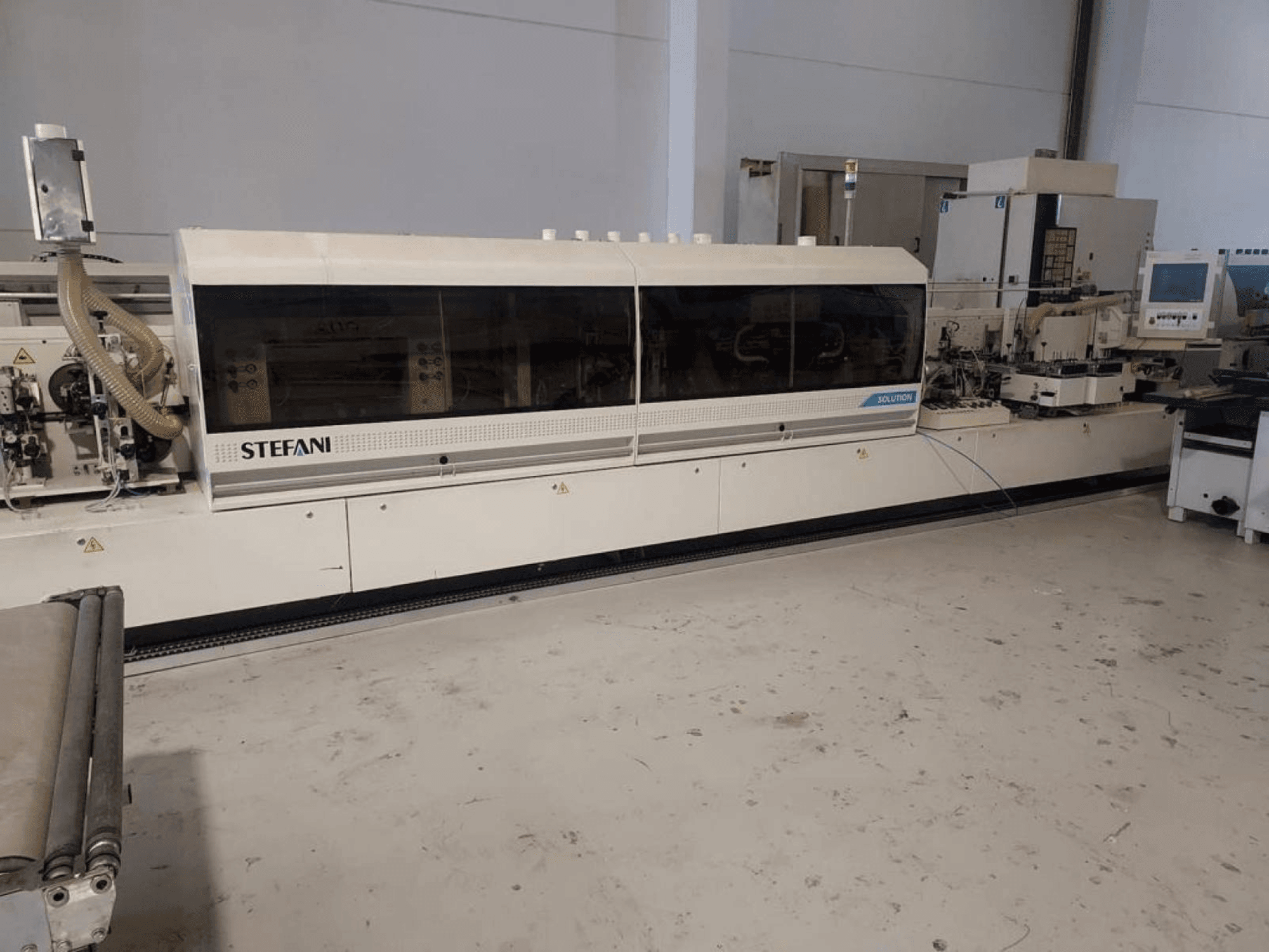 Máquina de aplicação de fita de borda da Stefani Solutions, vista frontal, com sistema de extração de pó e painel de controlo visíveis, numa oficina.