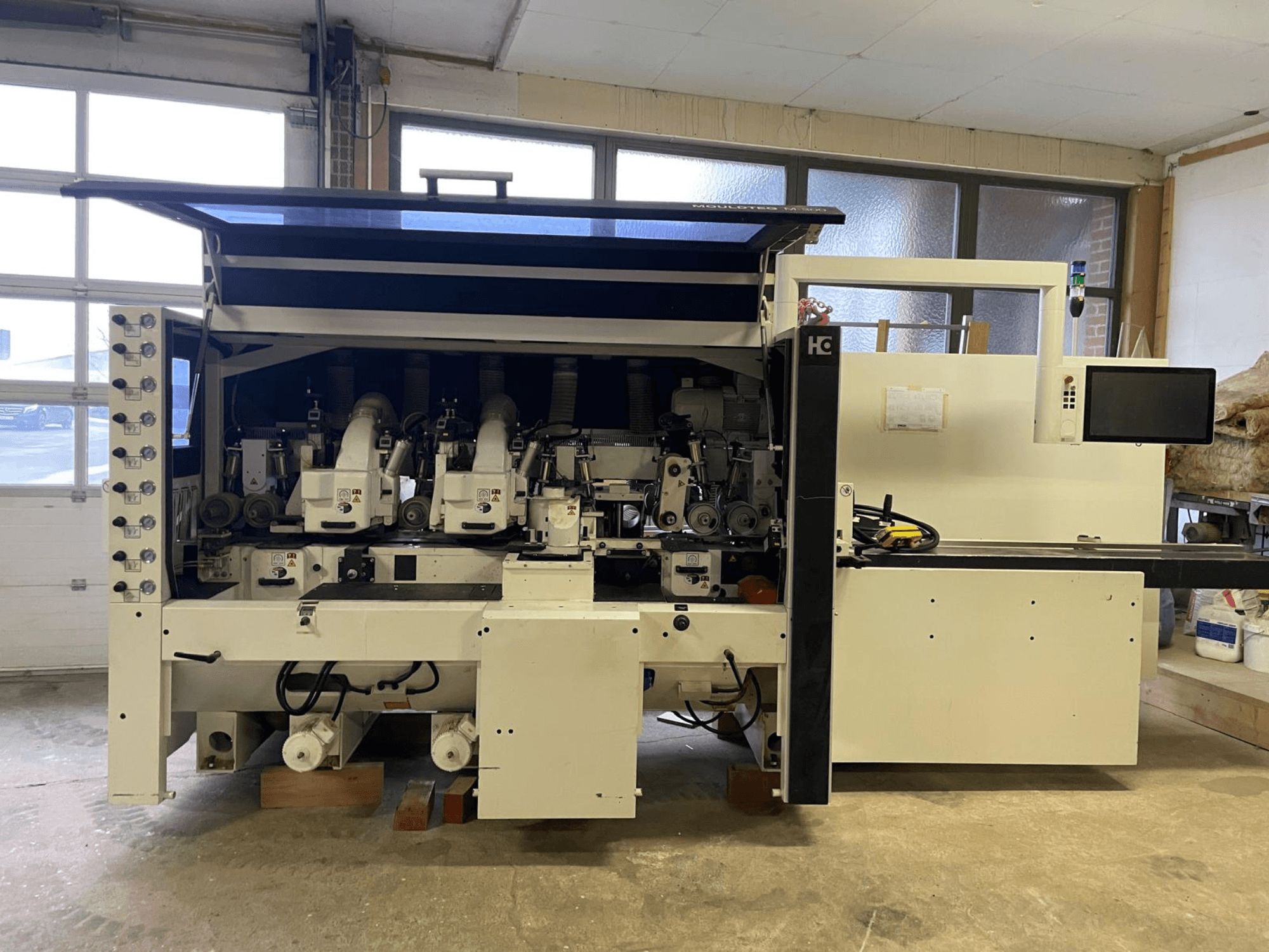 Máquina CNC Häwa, vista frontal, com vários fusos, painel de controlo e mangueiras de extração de poeiras, adequada para o processamento de madeira.