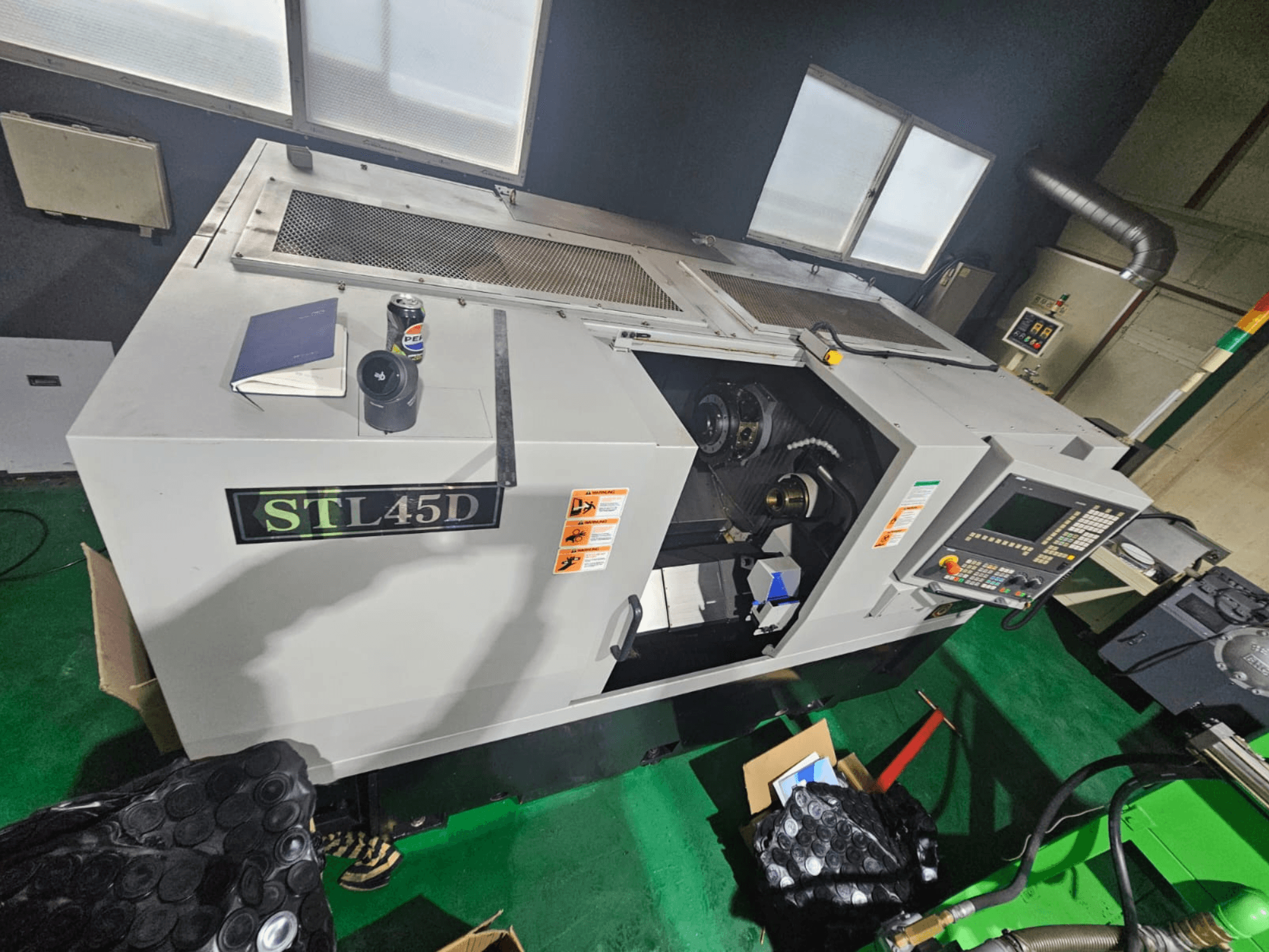 Máquina CNC STL45D vista de cima, mostrando o painel de controlo, a peça cilíndrica, o computador portátil e a lata no topo.