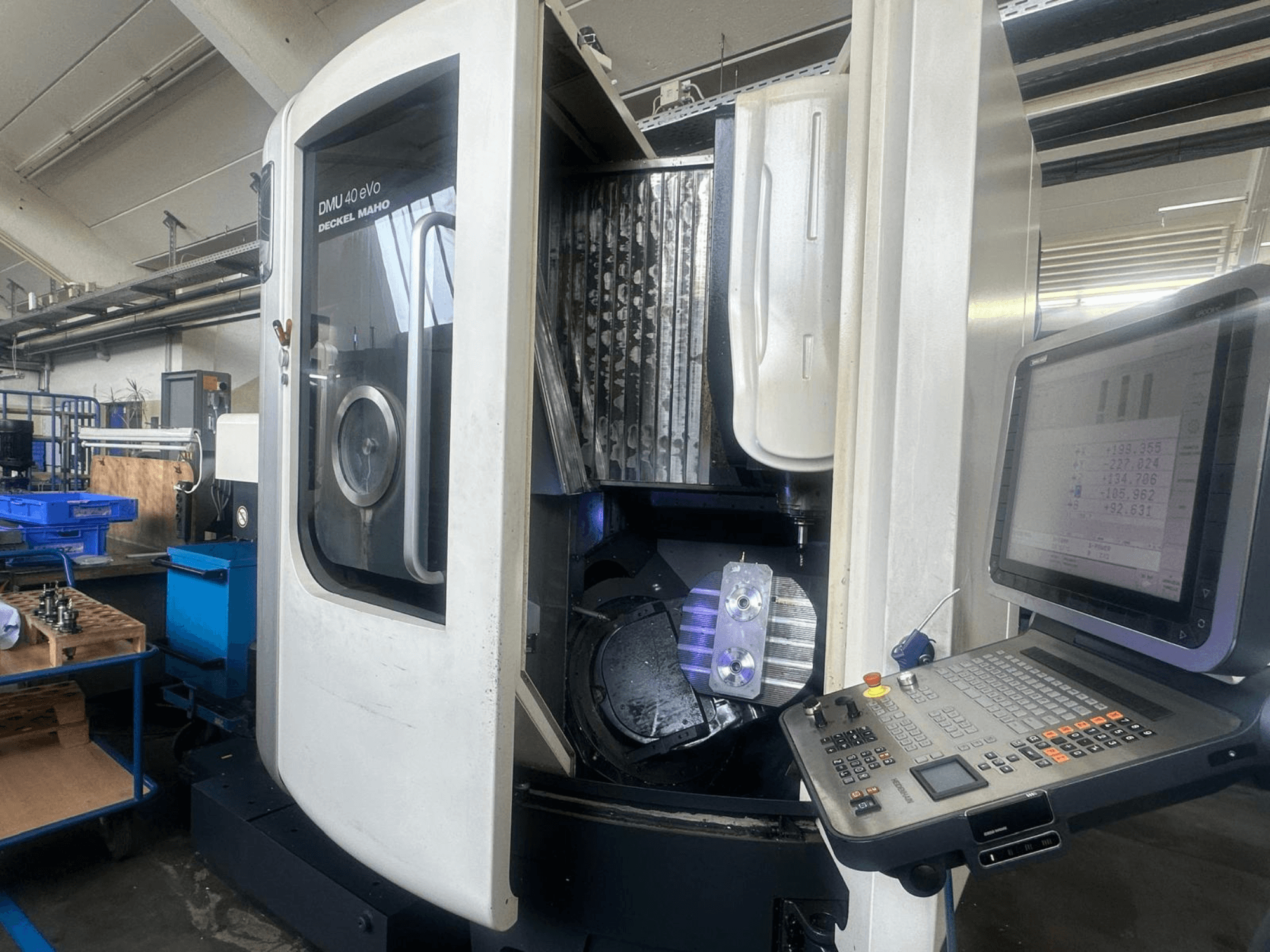 Fresadora DMU 40 eVo da Deckel Maho numa oficina, vista frontal, mostrando o painel de controlo e a peça metálica no fuso.