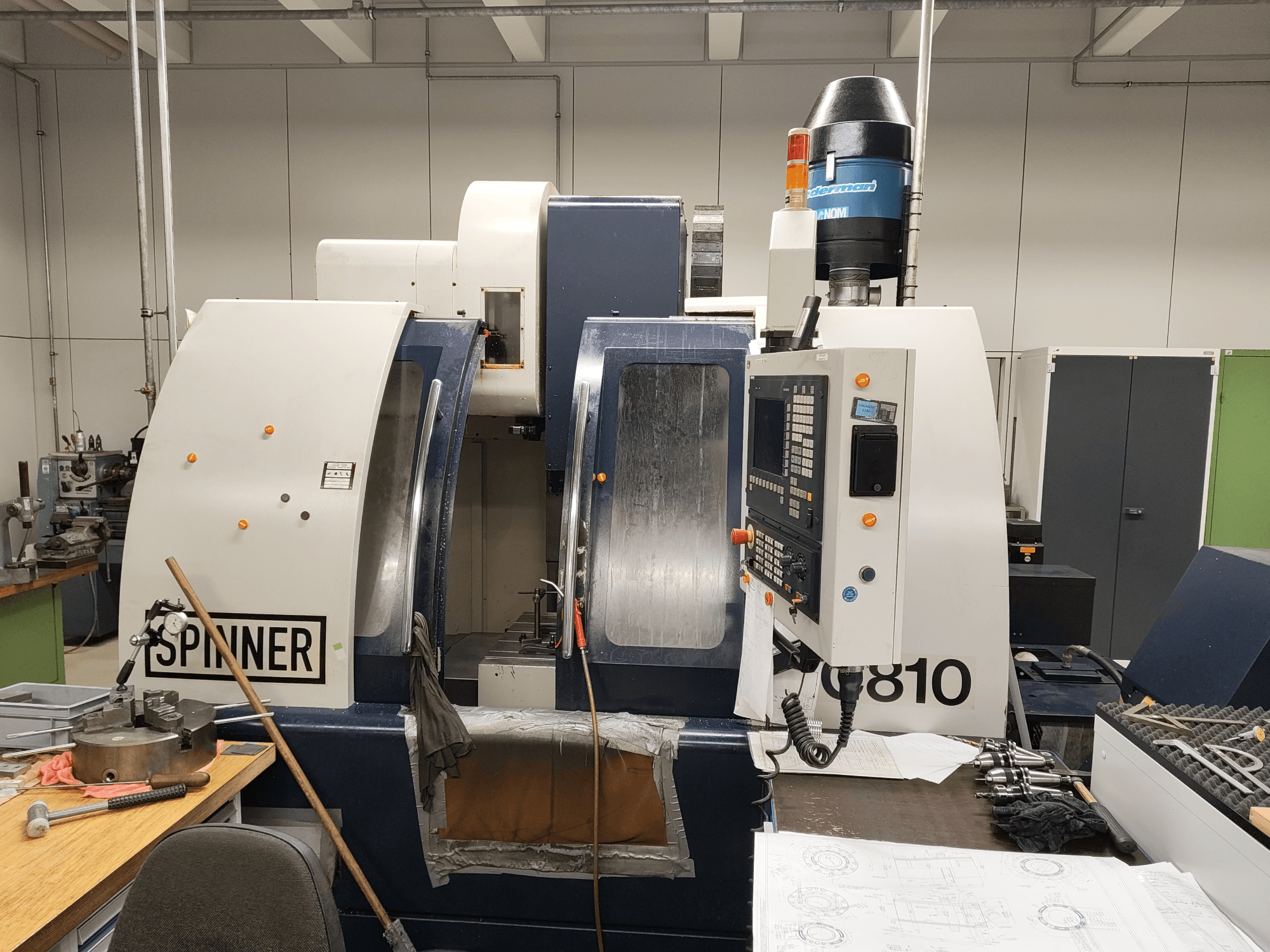 Centro de maquinagem vertical SPINNER VC810, vista frontal, mostrando o painel de controlo, a área de trabalho e as ferramentas acopladas.